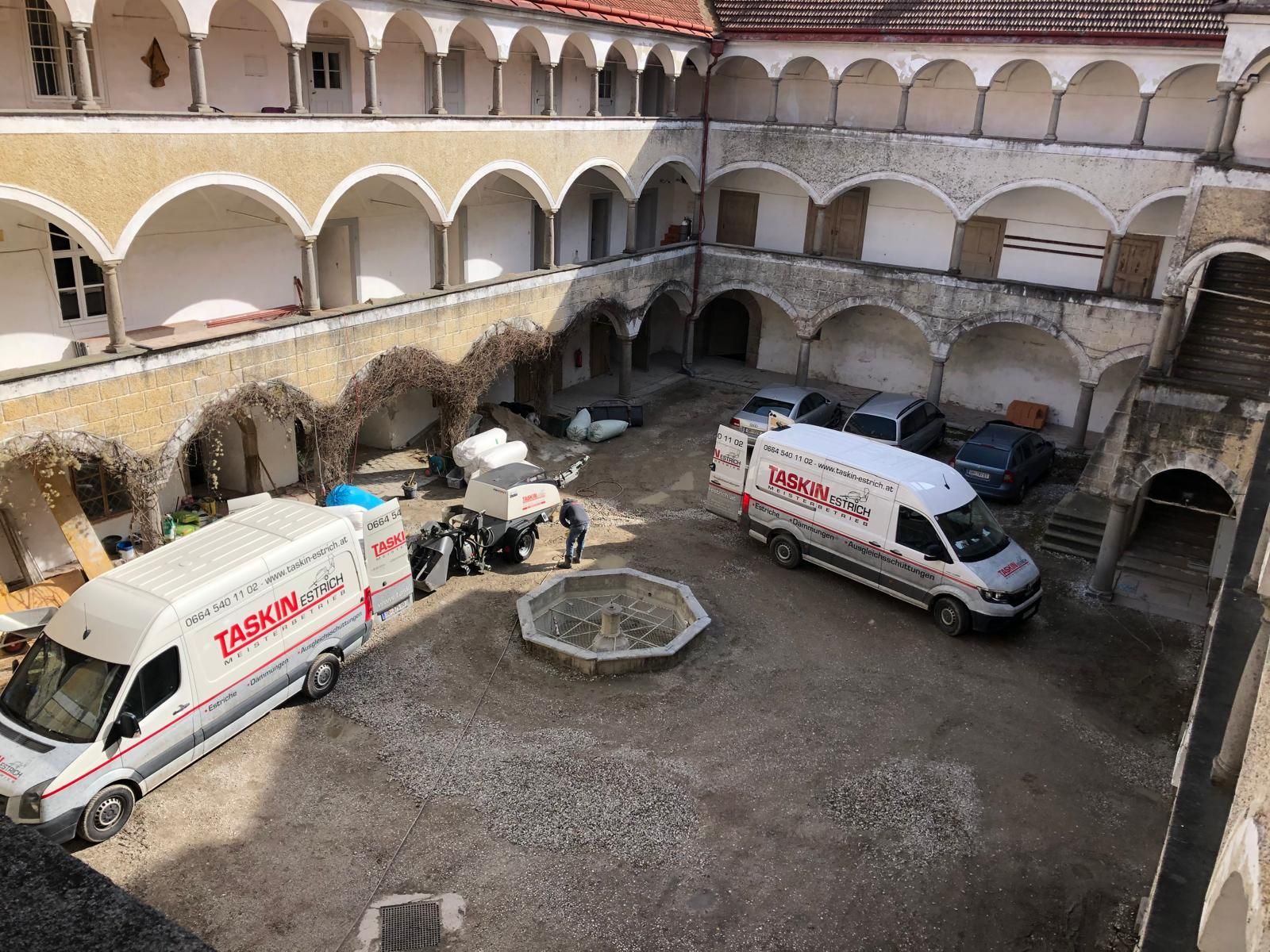 Zwei weiße Lieferwagen parken im Hof eines Gebäudes.