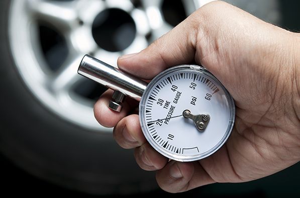 Une main tient un manomètre analogique argenté devant une roue de voiture floue.