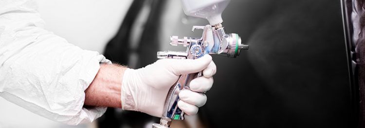 Une personne portant des gants blancs utilise un pistolet à peinture pour appliquer de la peinture sur une surface foncée.