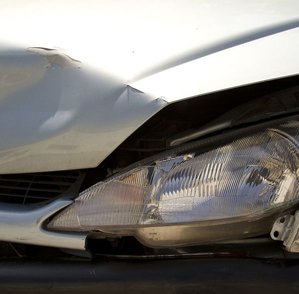 Gros plan sur une voiture argentée présentant des dommages à l'avant, notamment un capot cabossé, un phare mal aligné et un pare-chocs cassé.