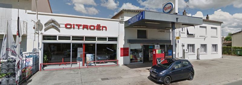 Une concession Citroën avec garage et station-service attenante, située dans un bâtiment blanc sous un ciel nuageux.