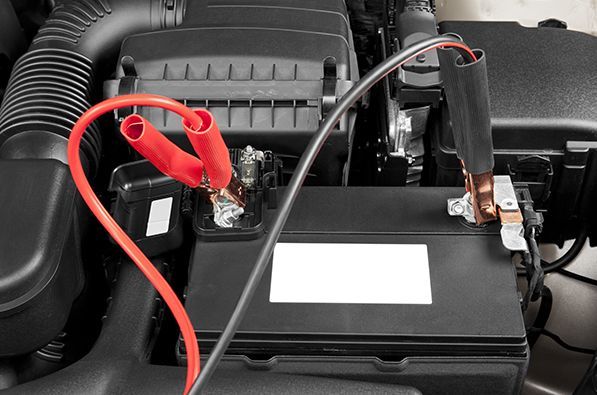 Des câbles de démarrage rouges et noirs connectés à une batterie de voiture sous le capot d'un véhicule.