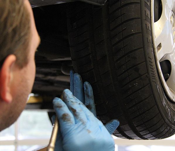Une personne portant des gants bleus inspecte la bande de roulement d'un pneu de voiture à l'aide d'un outil.