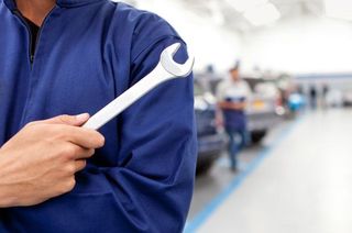 Une personne en uniforme bleu tient une clé à molette dans un atelier de réparation automobile lumineux et flou.