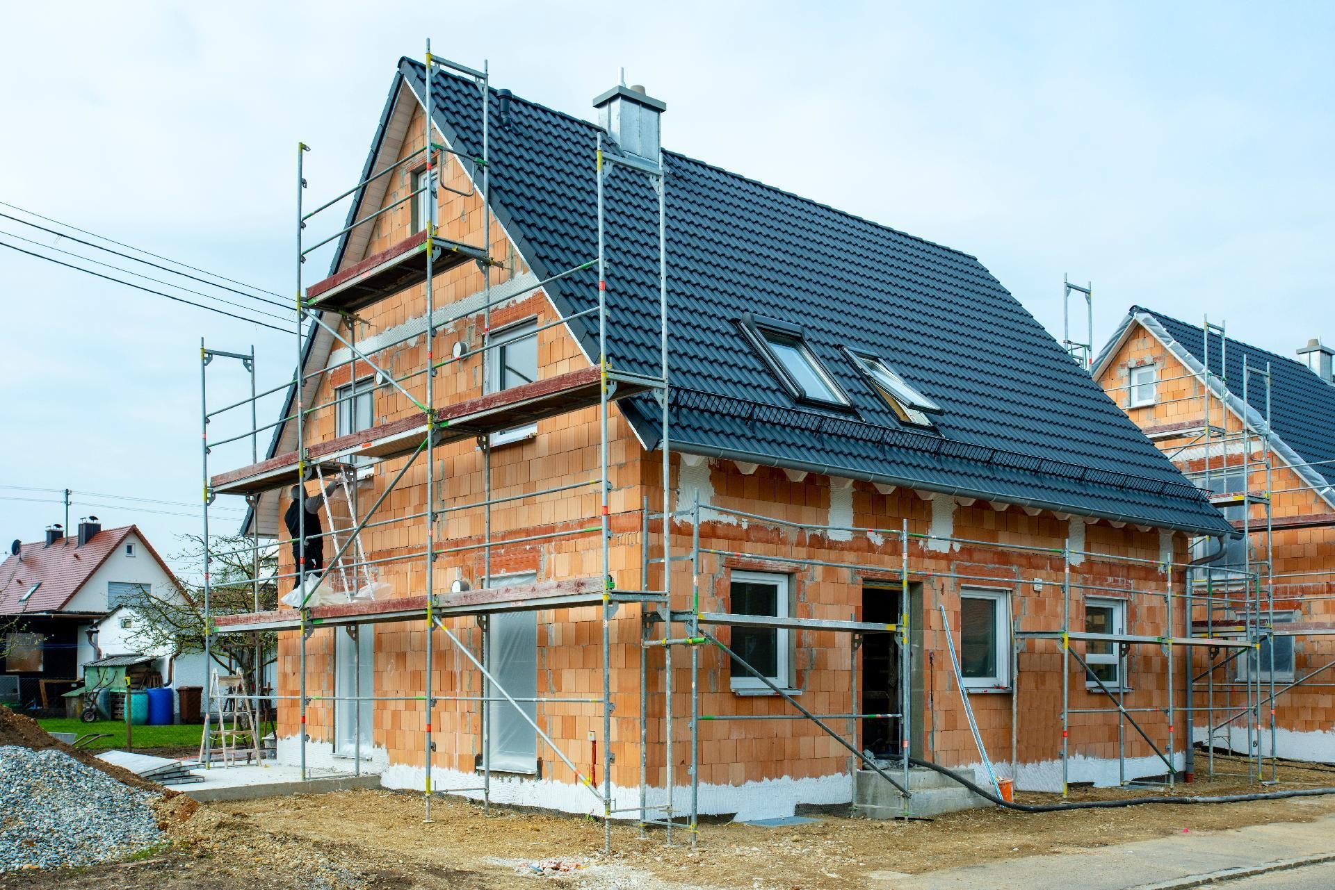 Haus im Bau mit Gerüst; freiliegendes Backsteinmauerwerk an der Fassade, schwarzes Dach.