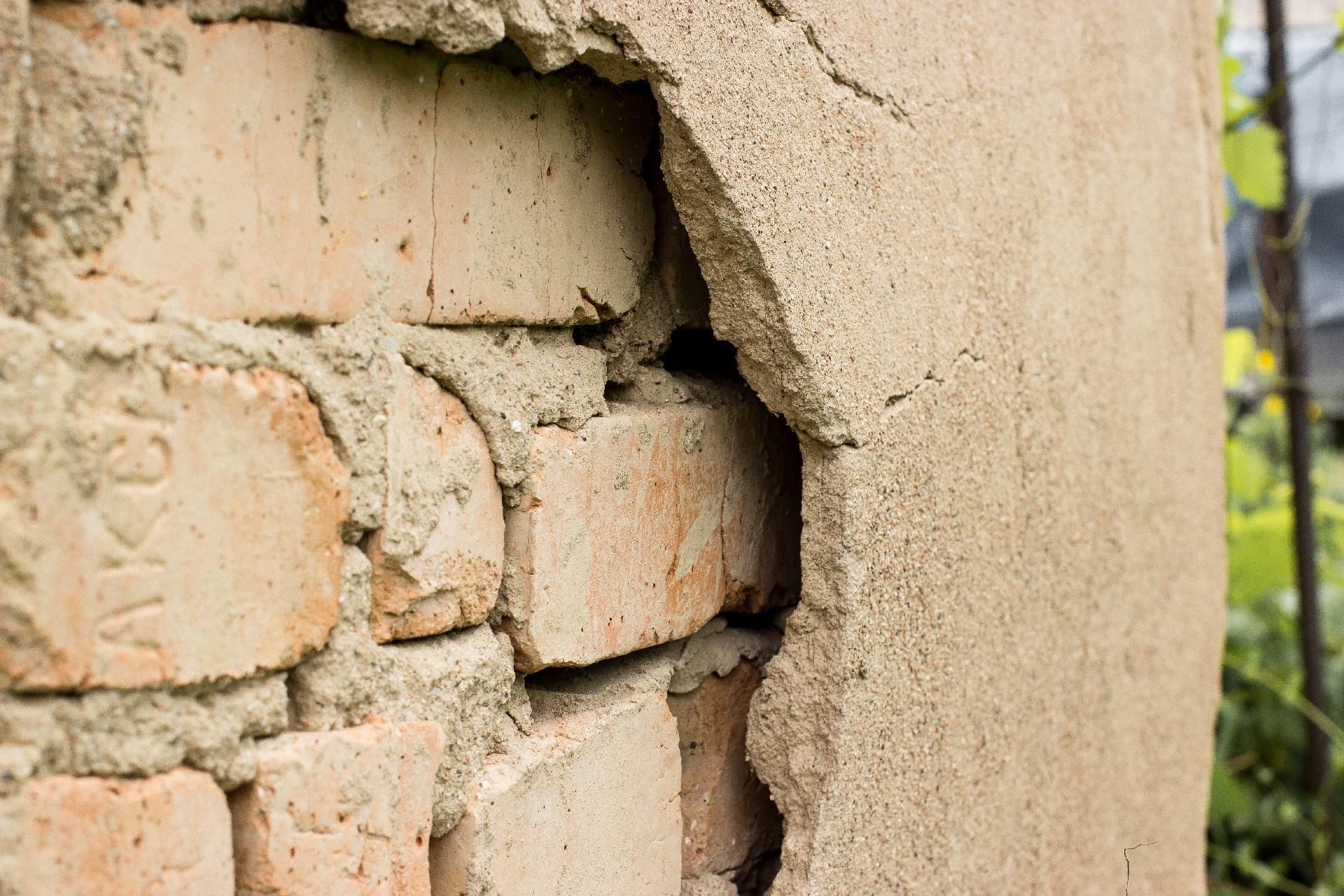 Backsteinmauer mit bröckelndem Putz, unter der die rotbraunen Ziegelsteine ​​sichtbar werden.
