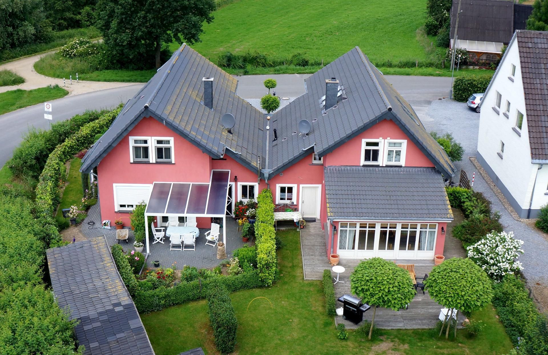 Rotes Haus mit dunklem Dach und Solarpaneelen, umgeben von Grün und Garten.