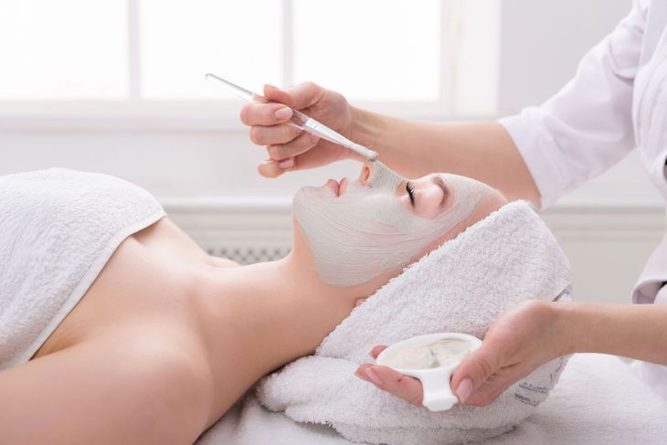 Eine Frau lässt sich in einem Spa eine Gesichtsmaske auftragen. Eine Kosmetikerin trägt die Maske mit einem Pinsel auf.