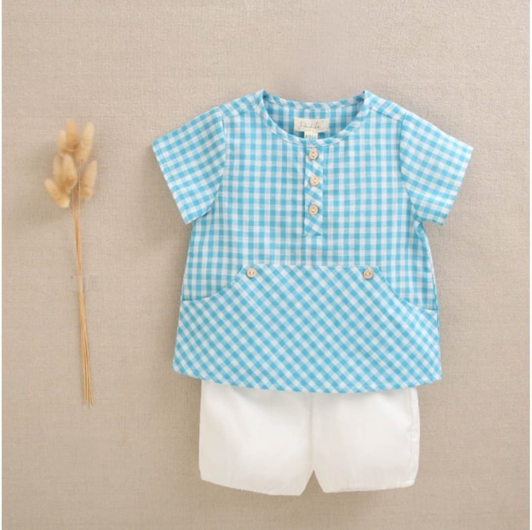 Un bebé lleva una camisa a cuadros azul y blanca y pantalones cortos blancos.
