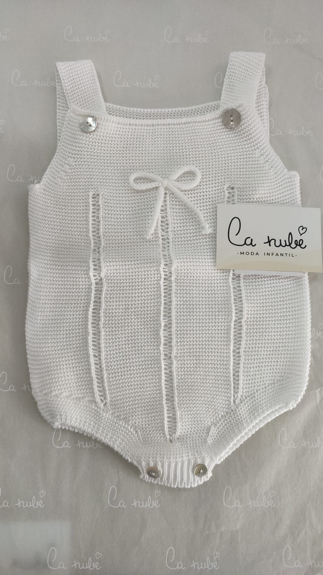 Un mono de bebé de punto blanco está sobre una mesa.