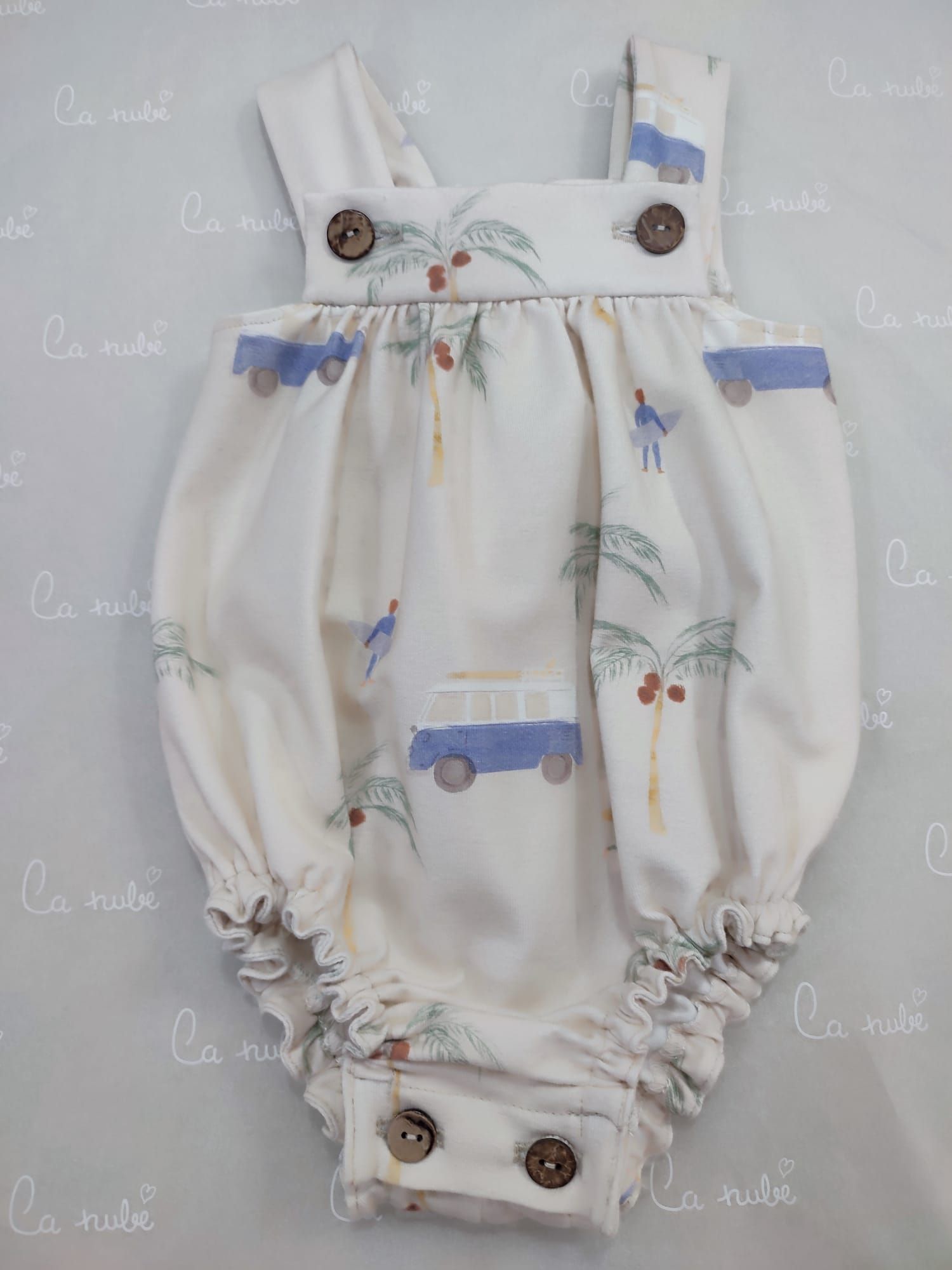 Un mono de bebé blanco con una furgoneta azul y palmeras.