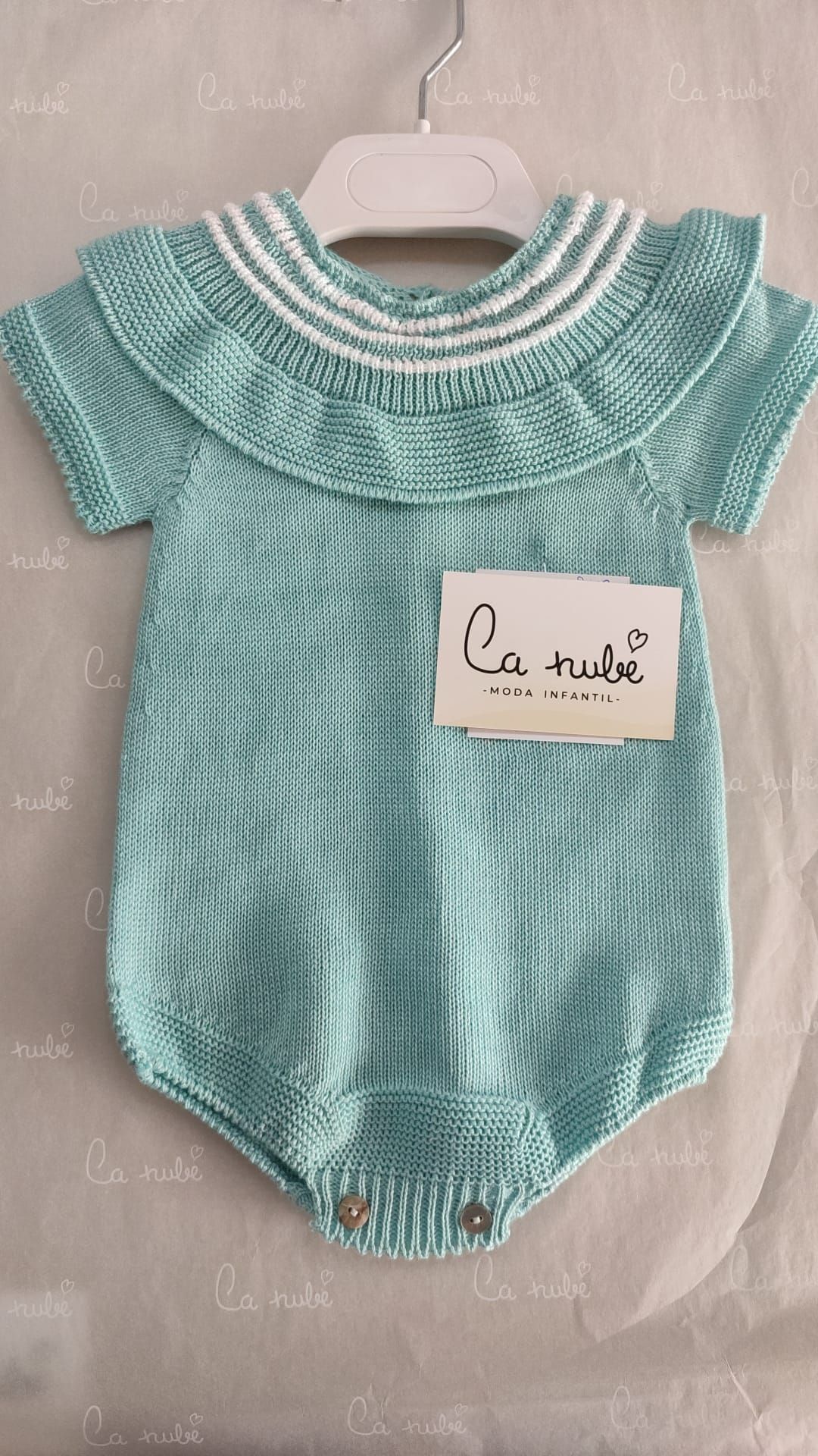 Un mono de bebé de punto verde está colgado en una percha.