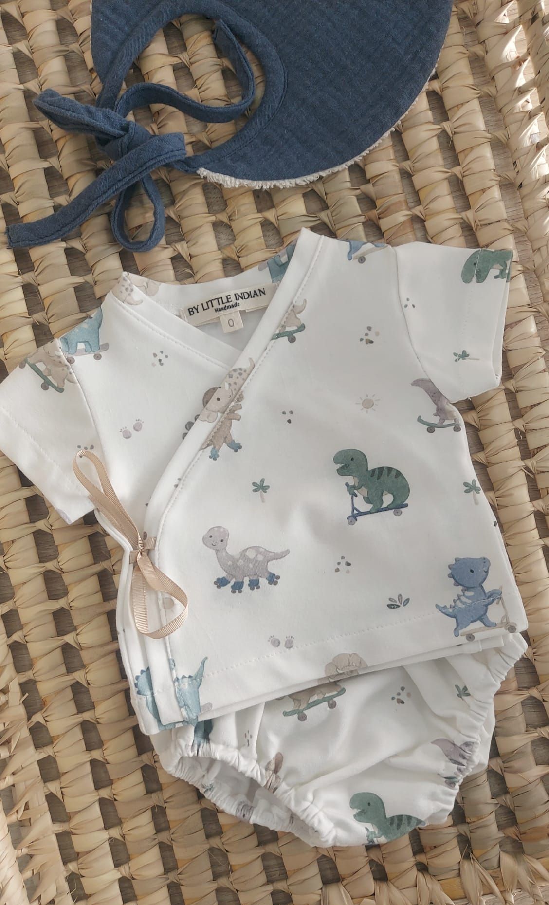 Un traje de bebé con dinosaurios está sobre una manta de mimbre.