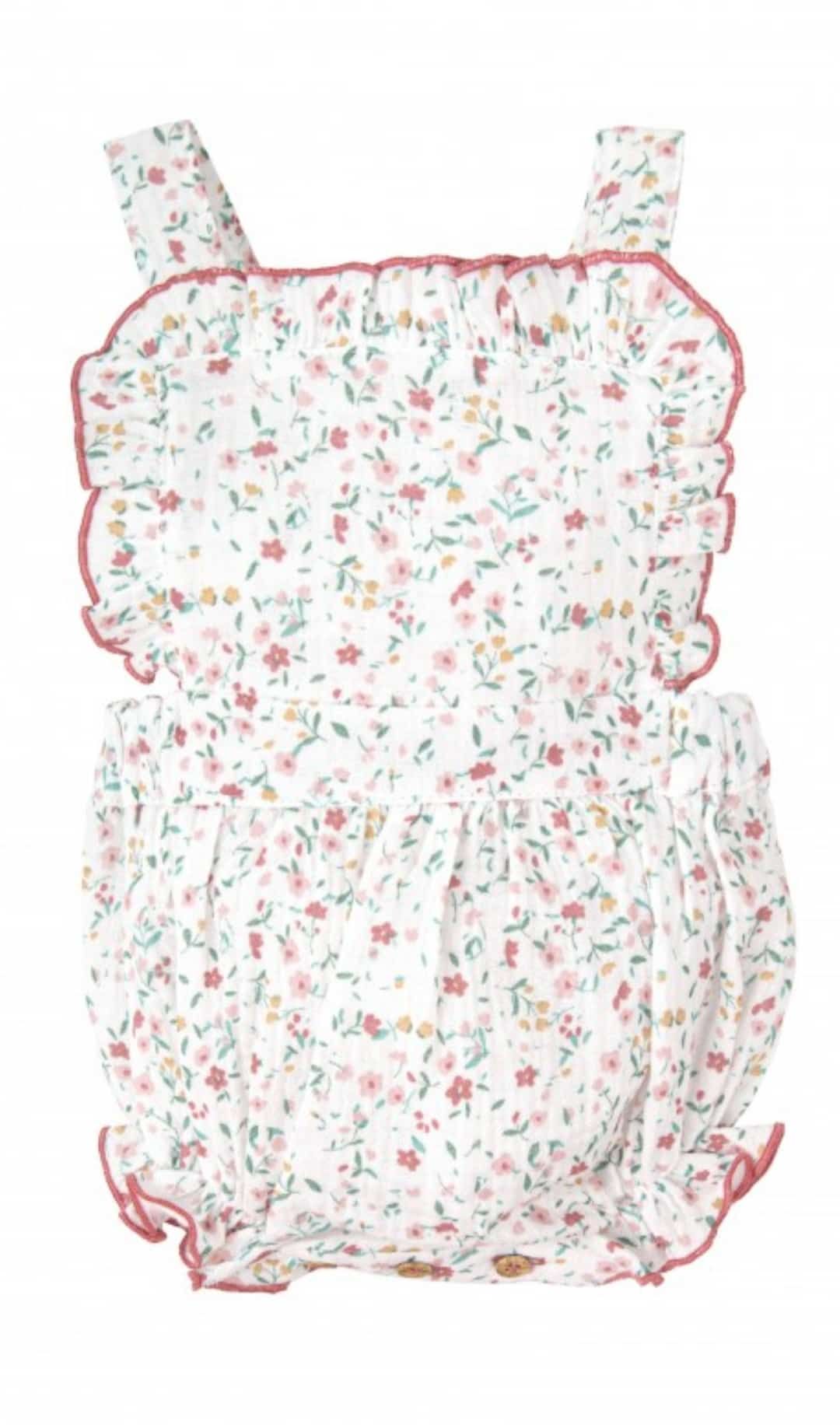 Un mono de bebé blanco con estampado floral y volantes sobre un fondo blanco.