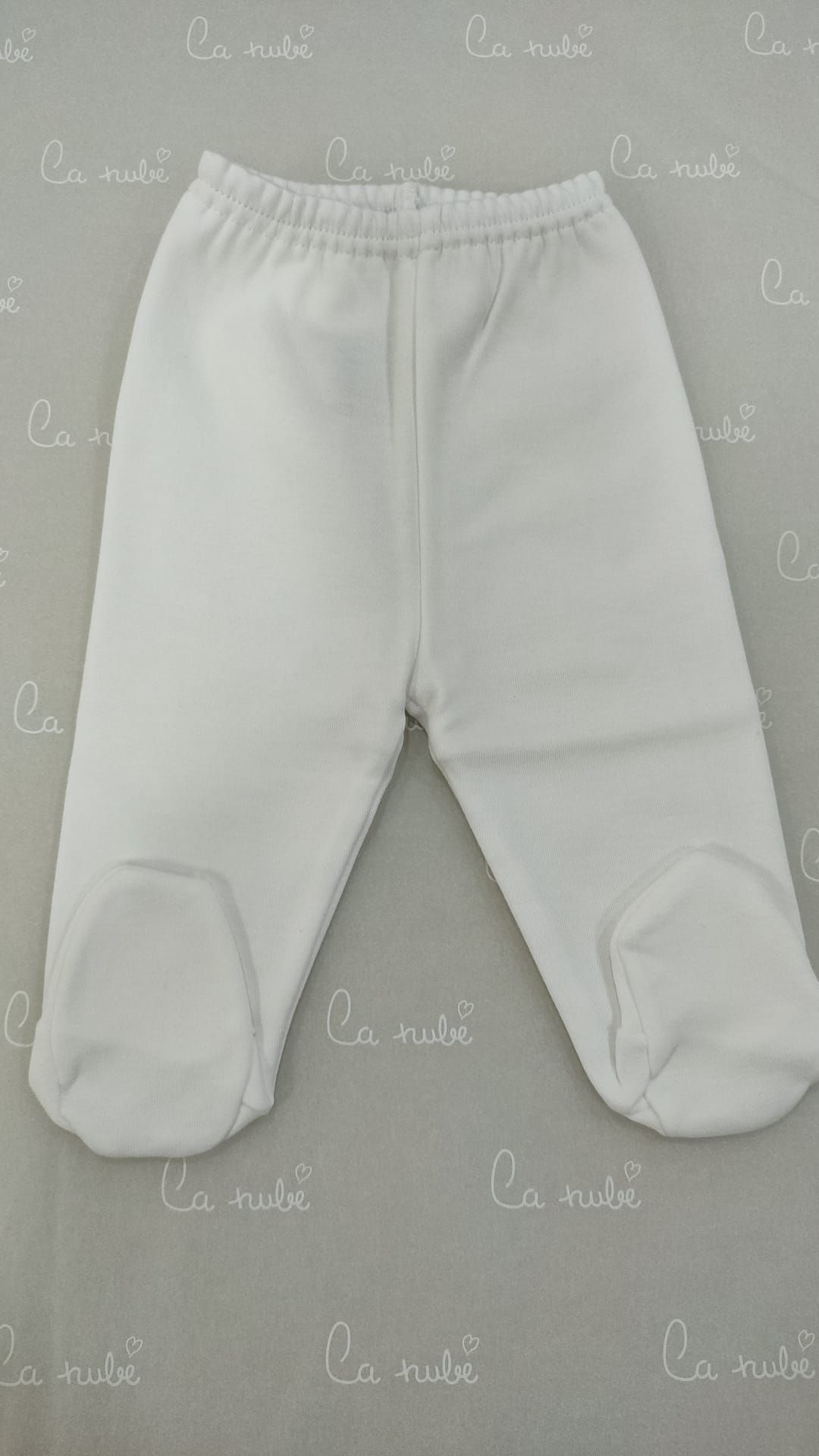 Un par de pantalones blancos de bebé con los pies sobre una mesa.