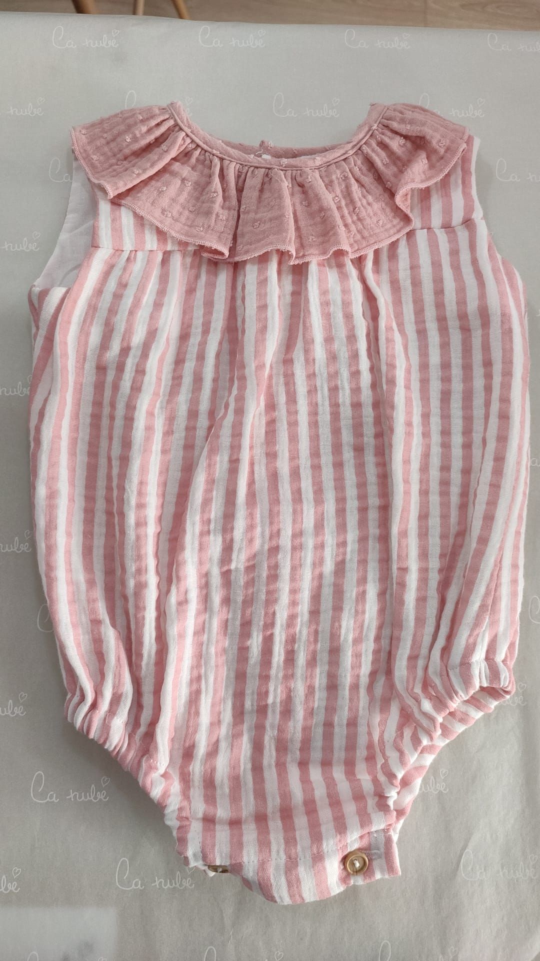 Un mono de bebé de rayas rosas y blancas con cuello con volantes está sobre una mesa.