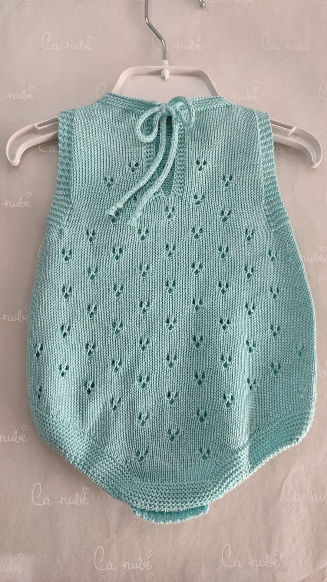 Un mono de bebé de punto verde cuelga de una percha blanca.