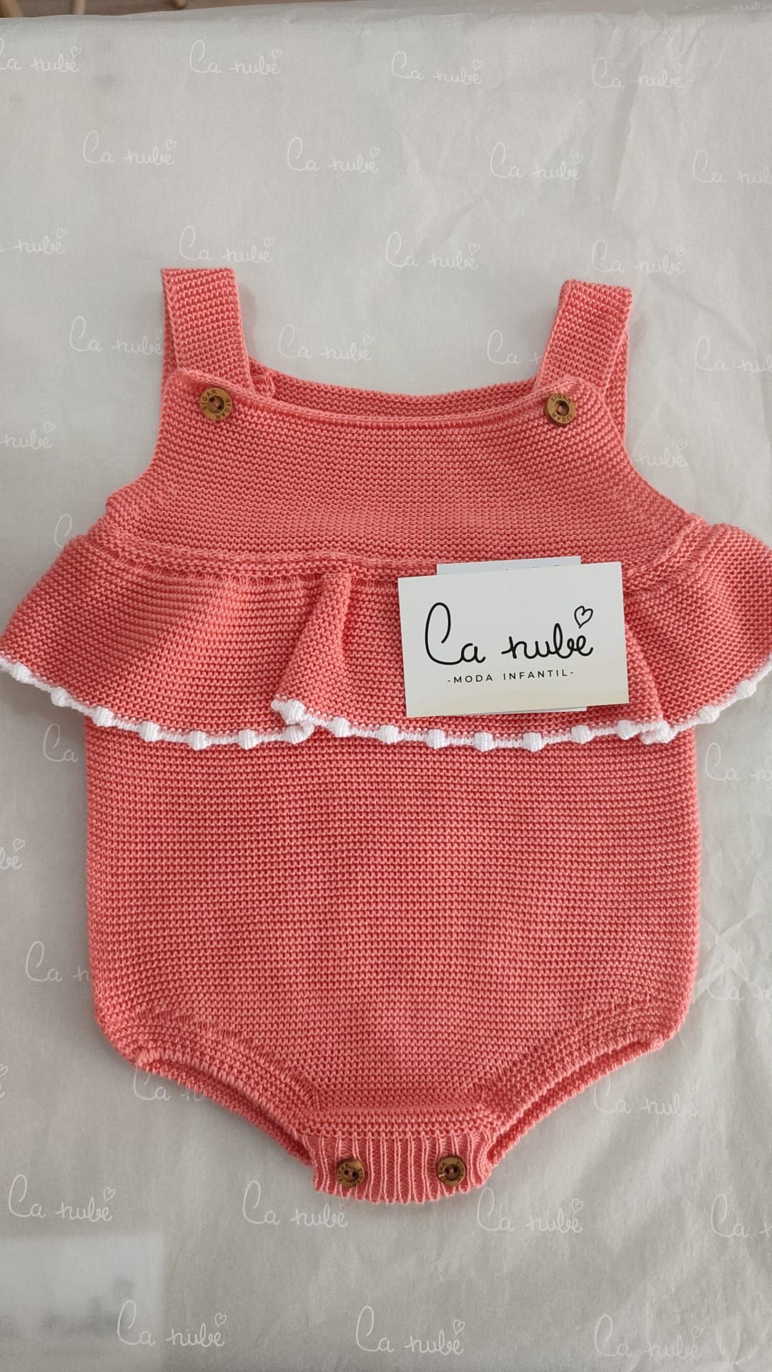 Un mono de bebé de punto rosa con volantes está sobre una mesa.