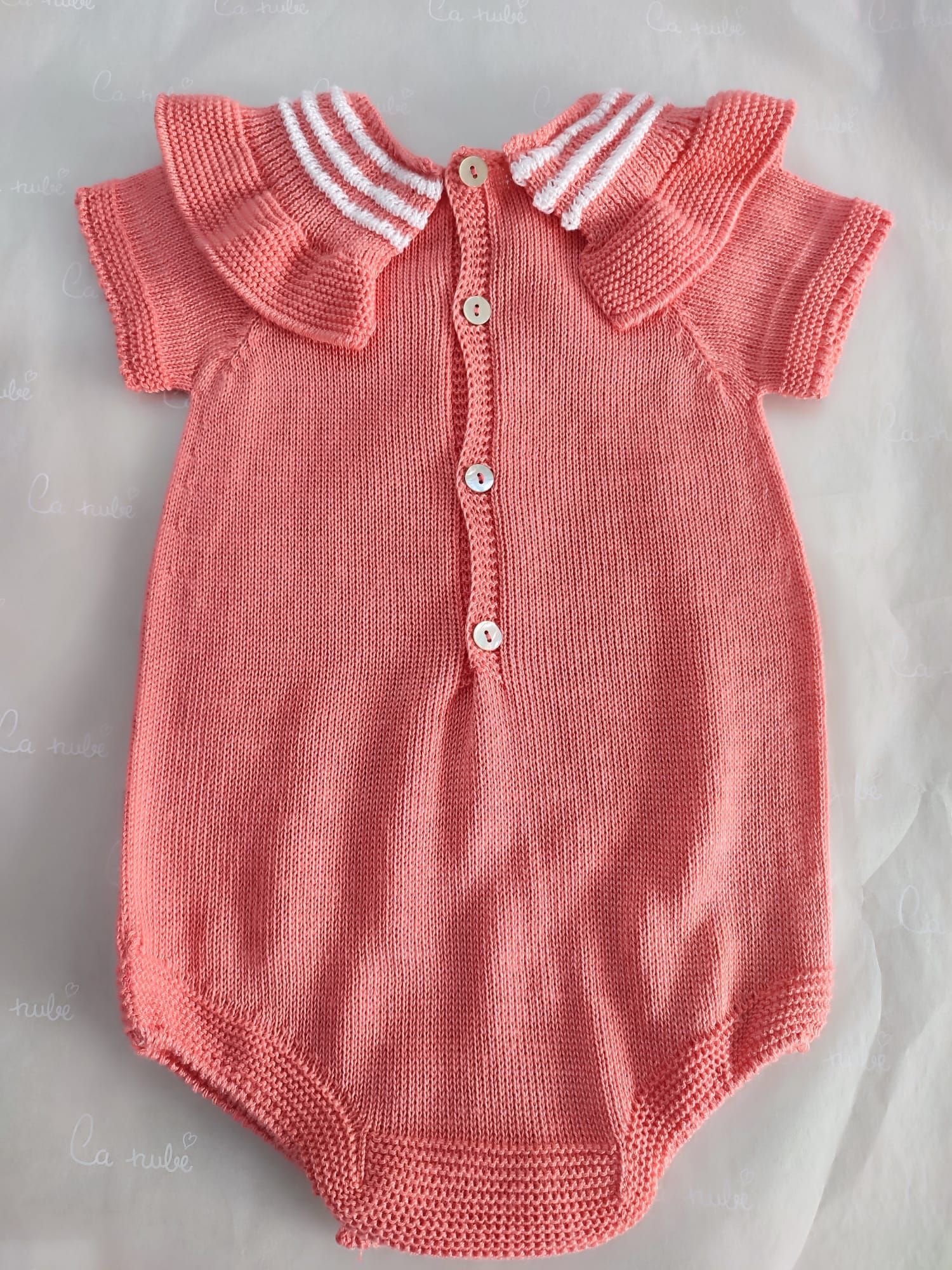 Un mono de bebé de punto rosa con cuello y botones blancos.