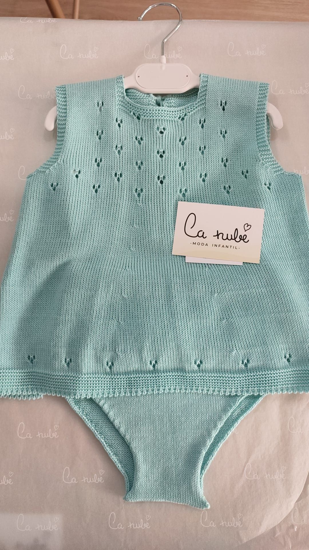 Un conjunto de punto de bebé está colgado en una percha.