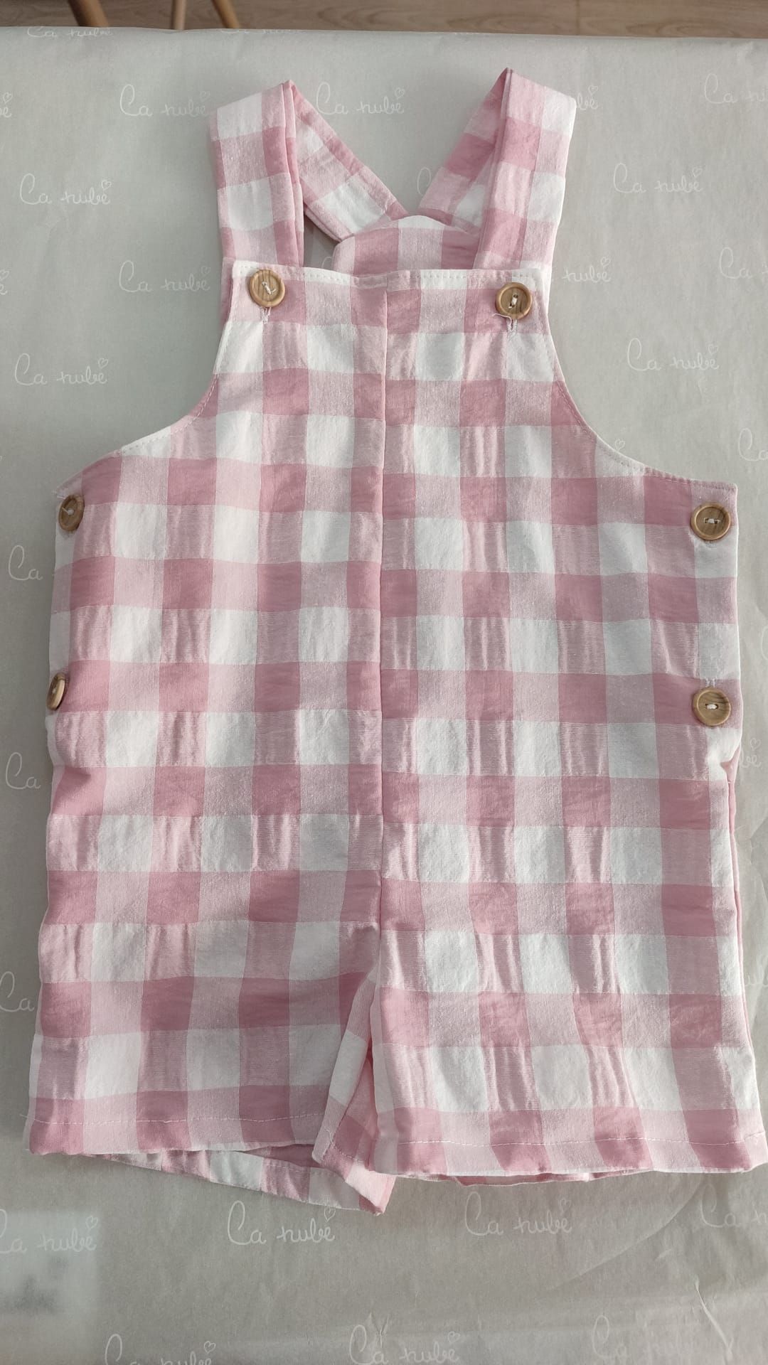 Una niña lleva un mono a cuadros rosa y blanco.