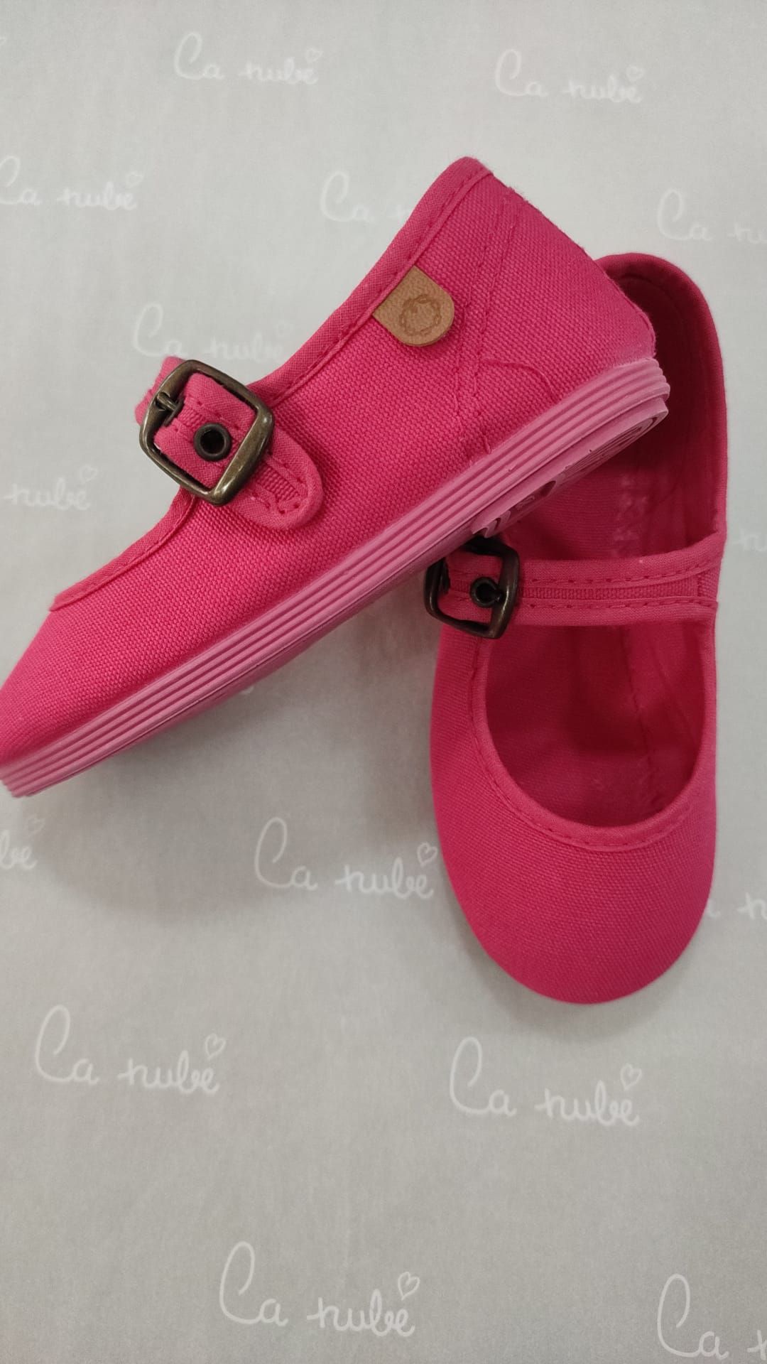 Un par de zapatos rosas con hebilla sobre una superficie blanca.