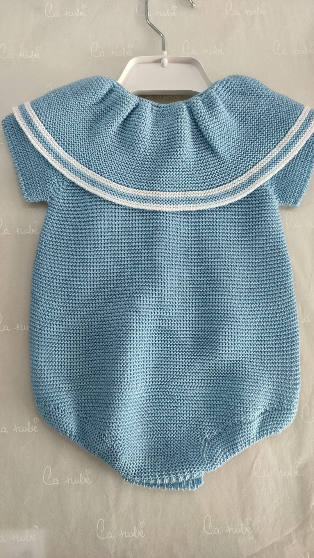 Un mono de bebé de punto azul con cuello blanco está colgado en una percha.