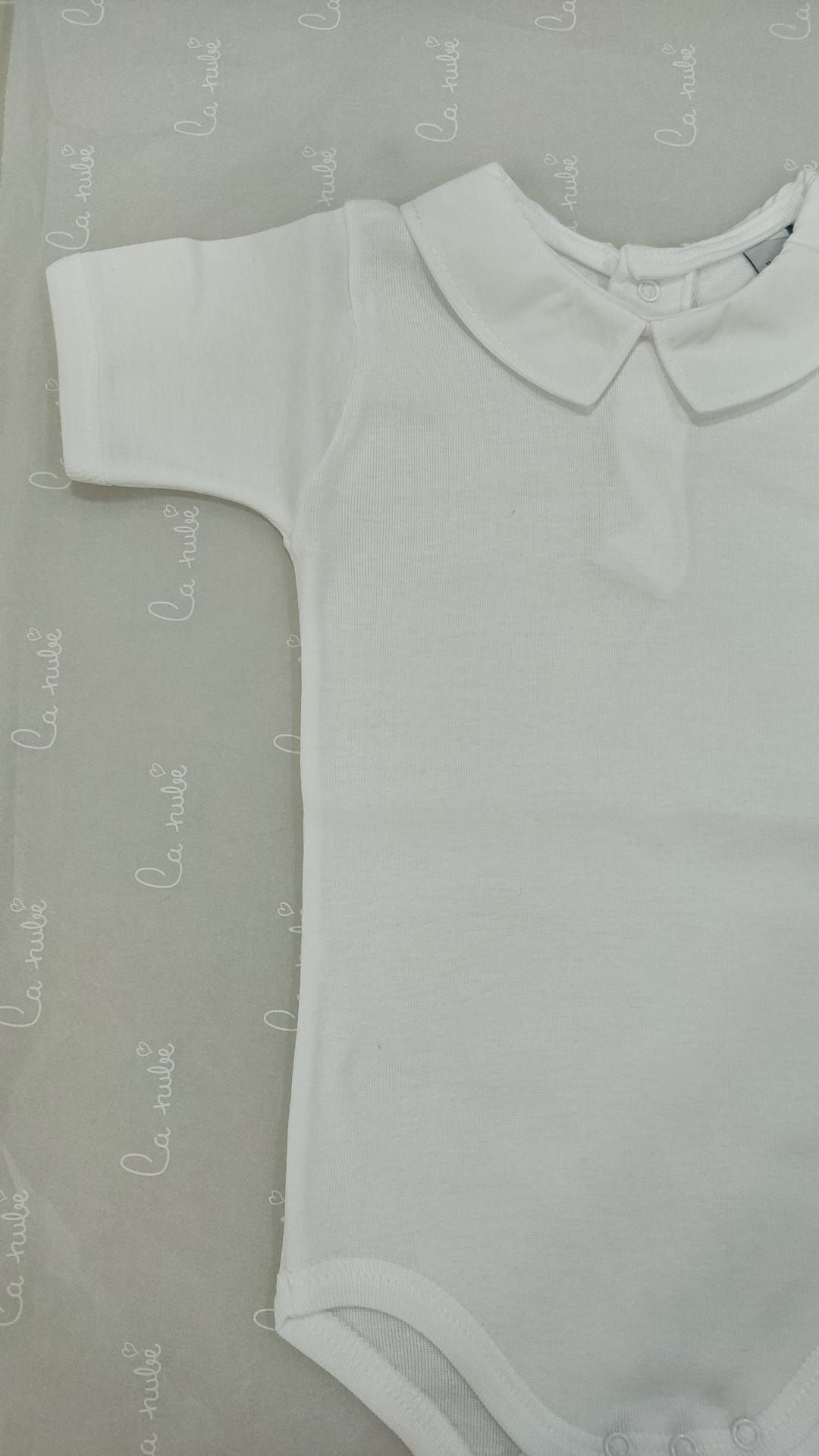 Un mono de bebé blanco con cuello está sentado en una cama.