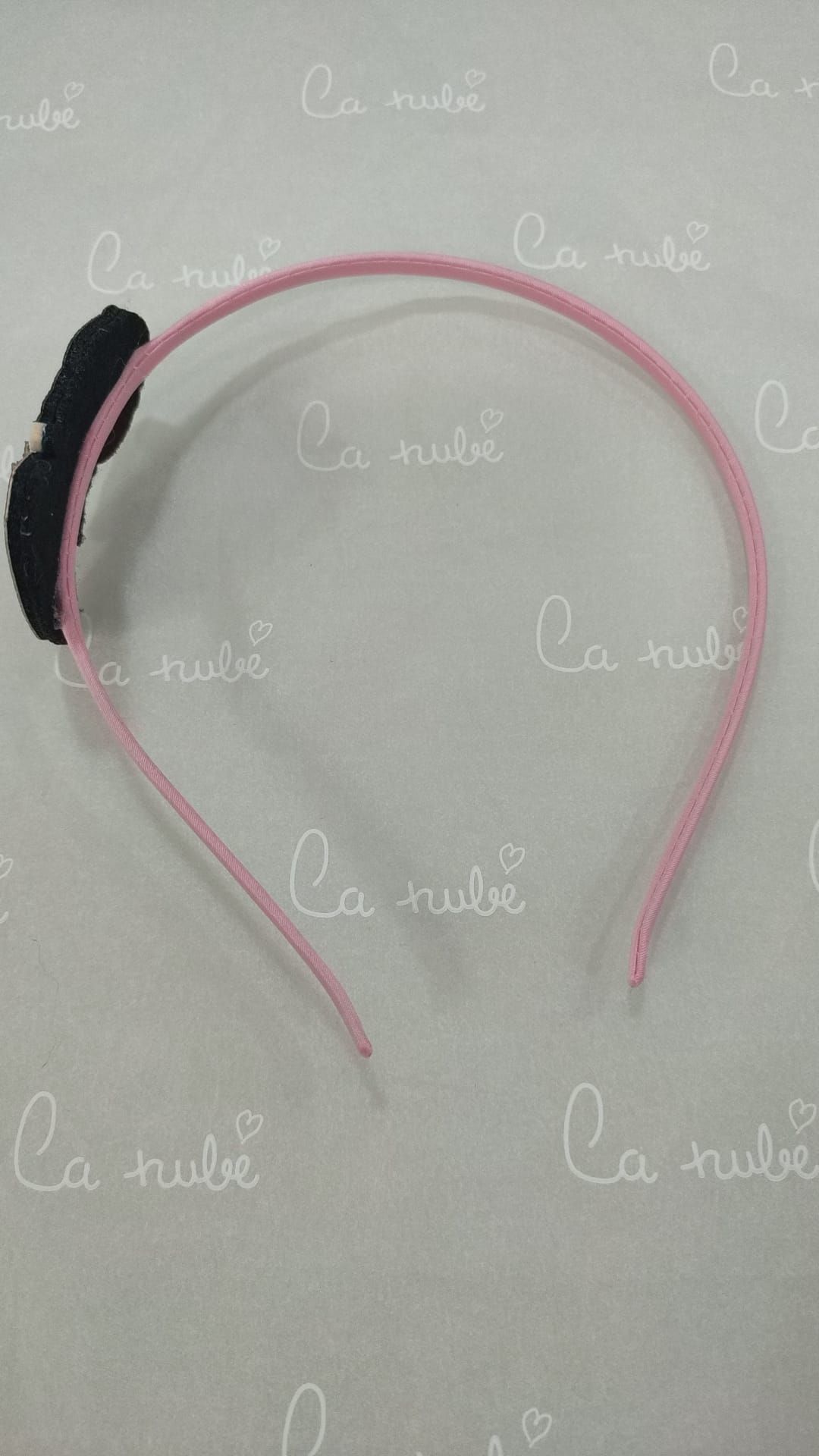 Una diadema rosa con un lazo negro reposa sobre una superficie blanca.