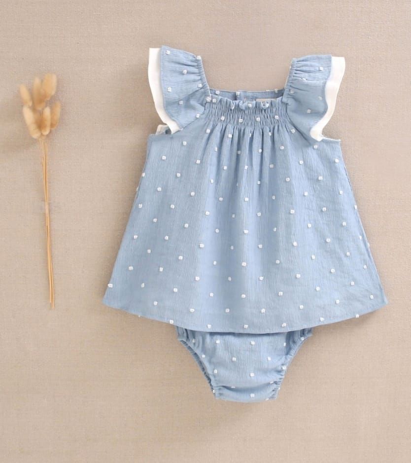 Una niña lleva un vestido azul con lunares blancos.