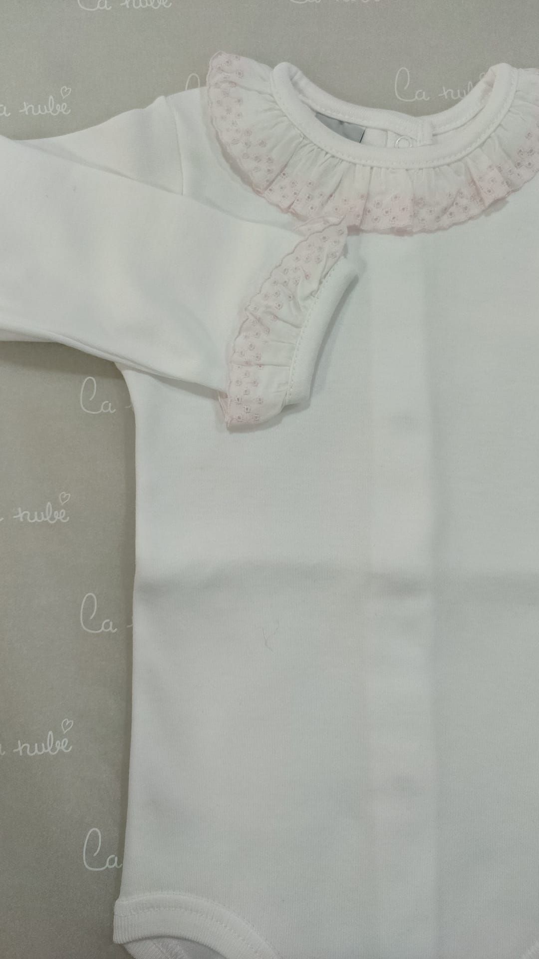 Una niña lleva un body blanco con un cuello con volantes de color rosa.