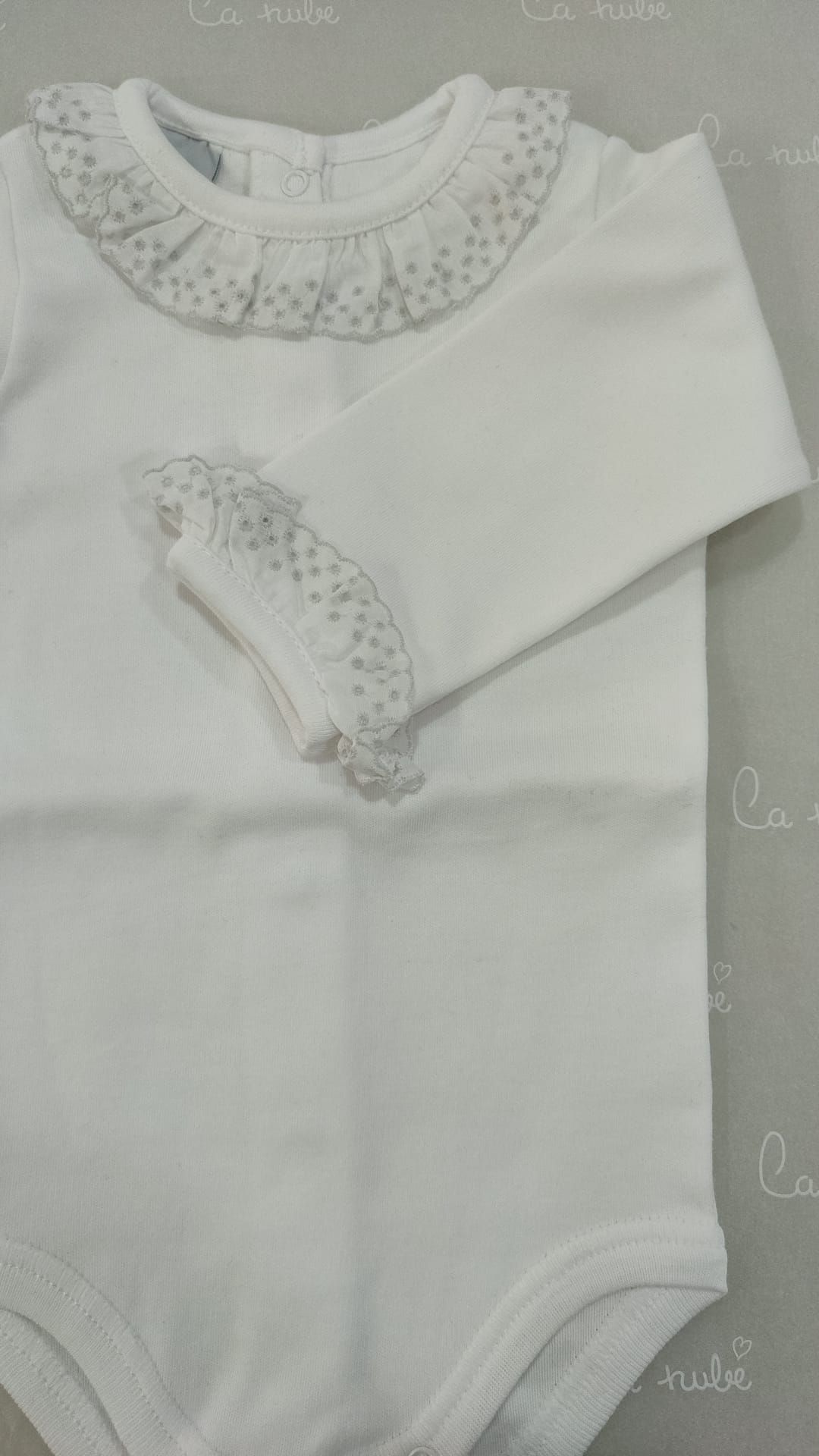Un mono de bebé blanco con cuello y mangas con volantes.