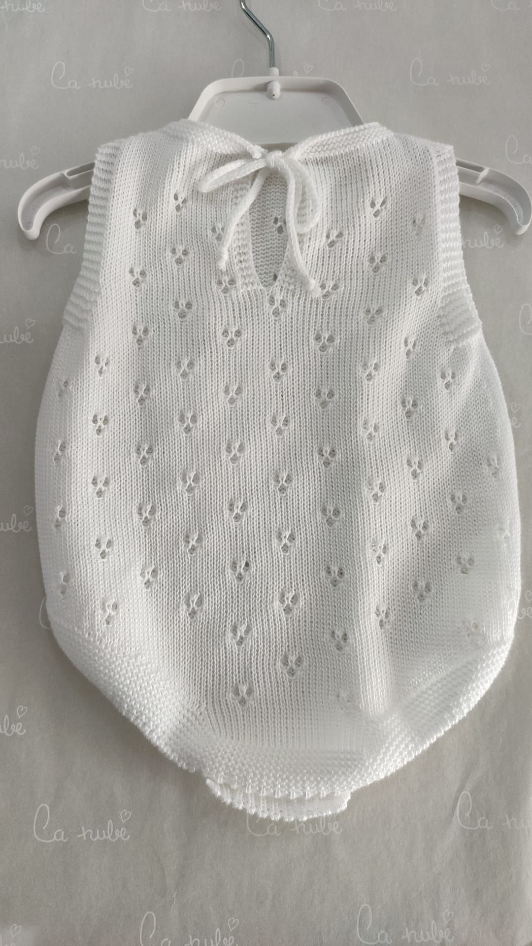 Un mono de bebé de punto blanco está colgado en una percha.