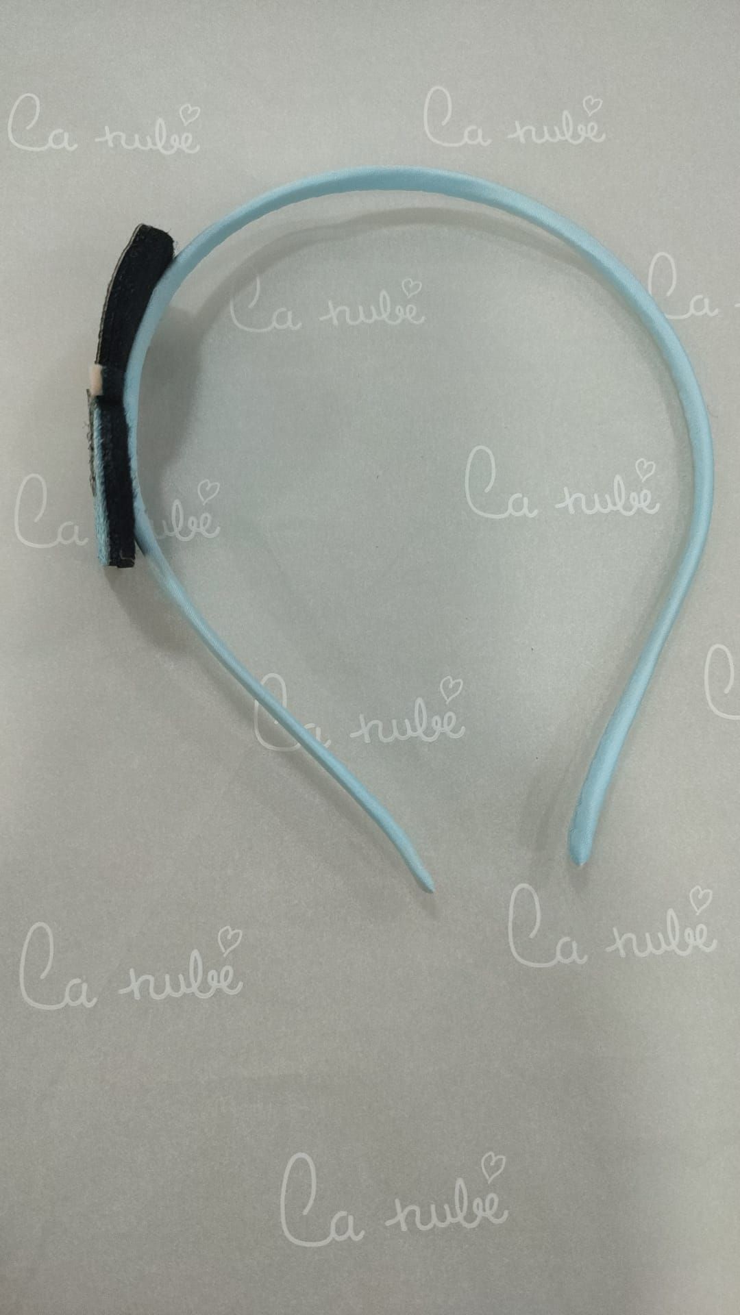 Una diadema azul con un lazo negro reposa sobre una superficie blanca.