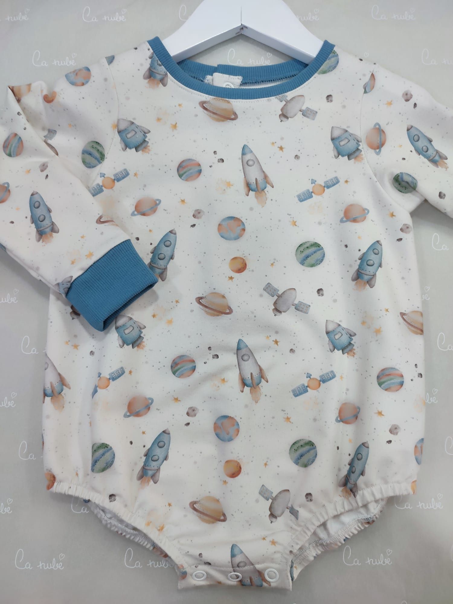 Un mono de bebé con cohetes y planetas está colgado en una percha.