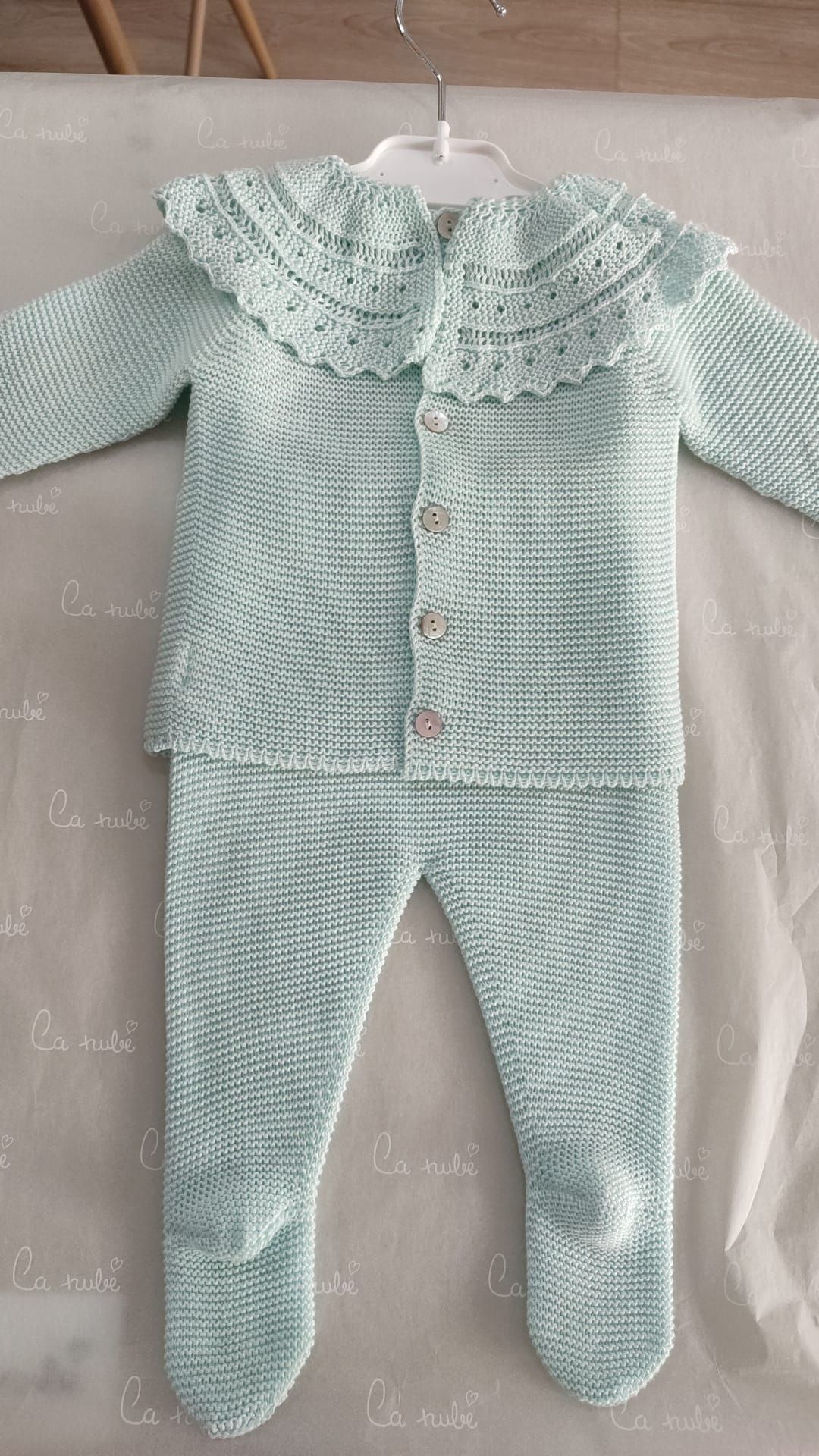 Un conjunto tejido de un bebé está sobre una cama.