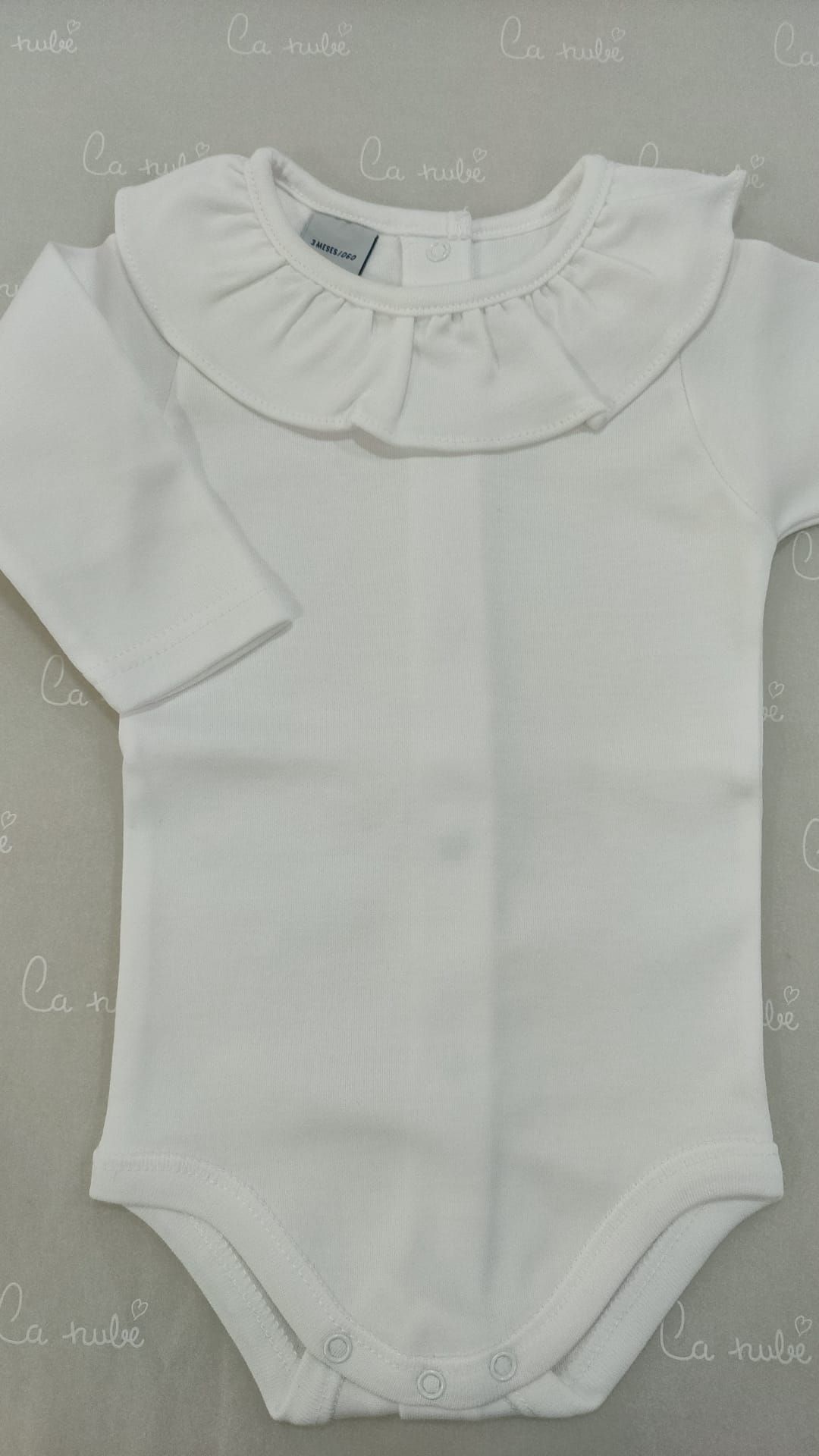 Un mono de bebé blanco con cuello con volantes y mangas largas.
