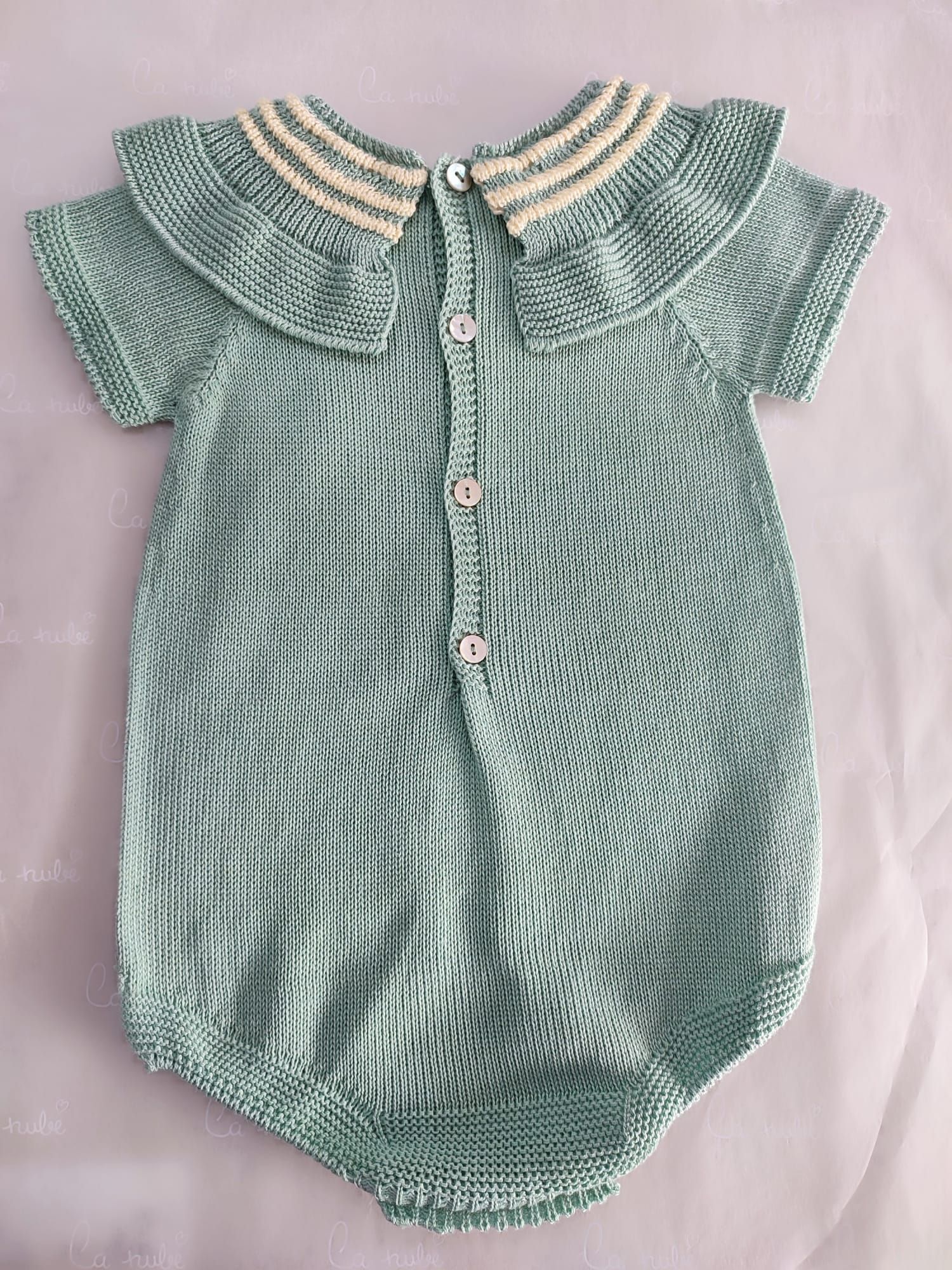 Un mono de bebé de punto verde con cuello y botones está sobre una cama.