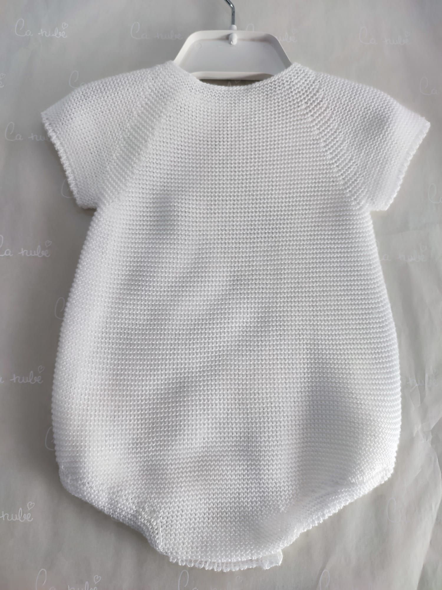 Un mono de bebé de punto blanco está colgado en una percha.