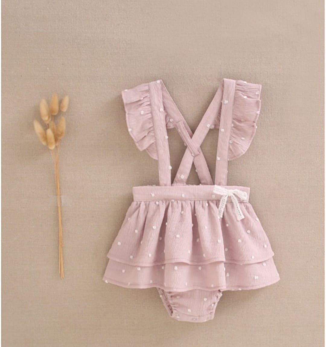 Una niña lleva un vestido rosa con volantes y tirantes.