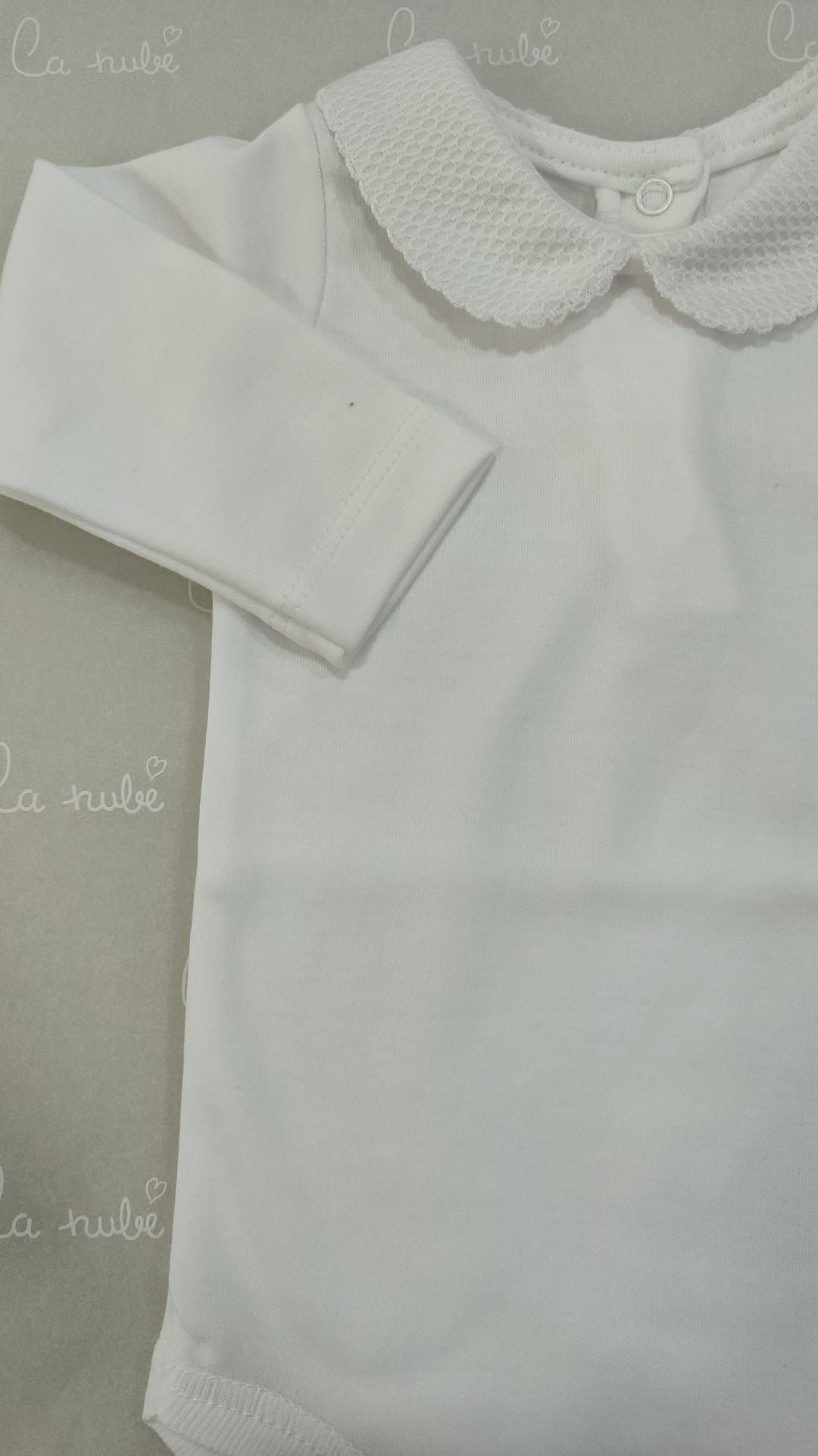 Un body de bebé blanco con cuello está sobre una mesa.