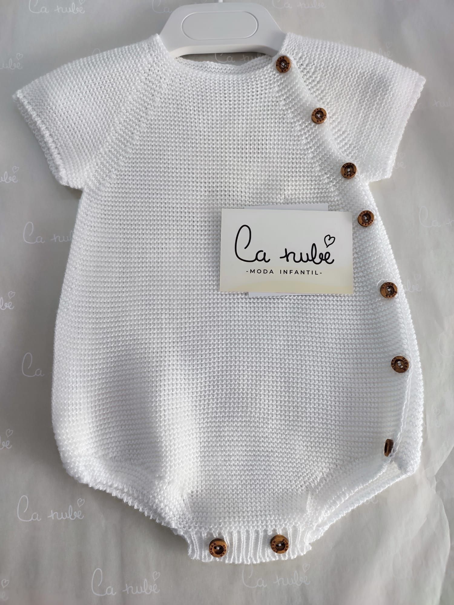 Un mono de bebé blanco con botones marrones está colgado en una percha.