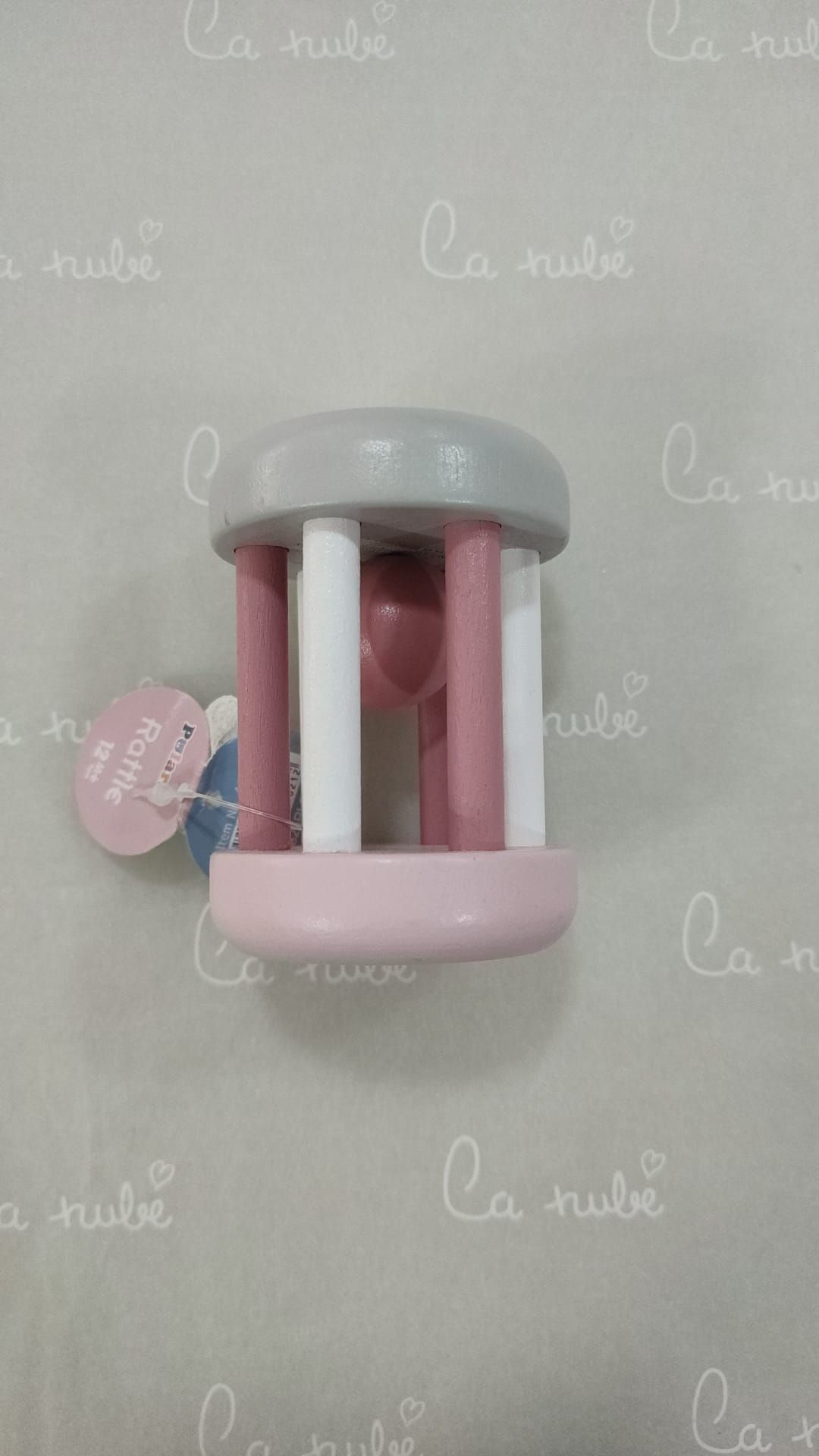 Un sonajero rosa y gris está sobre una superficie blanca.