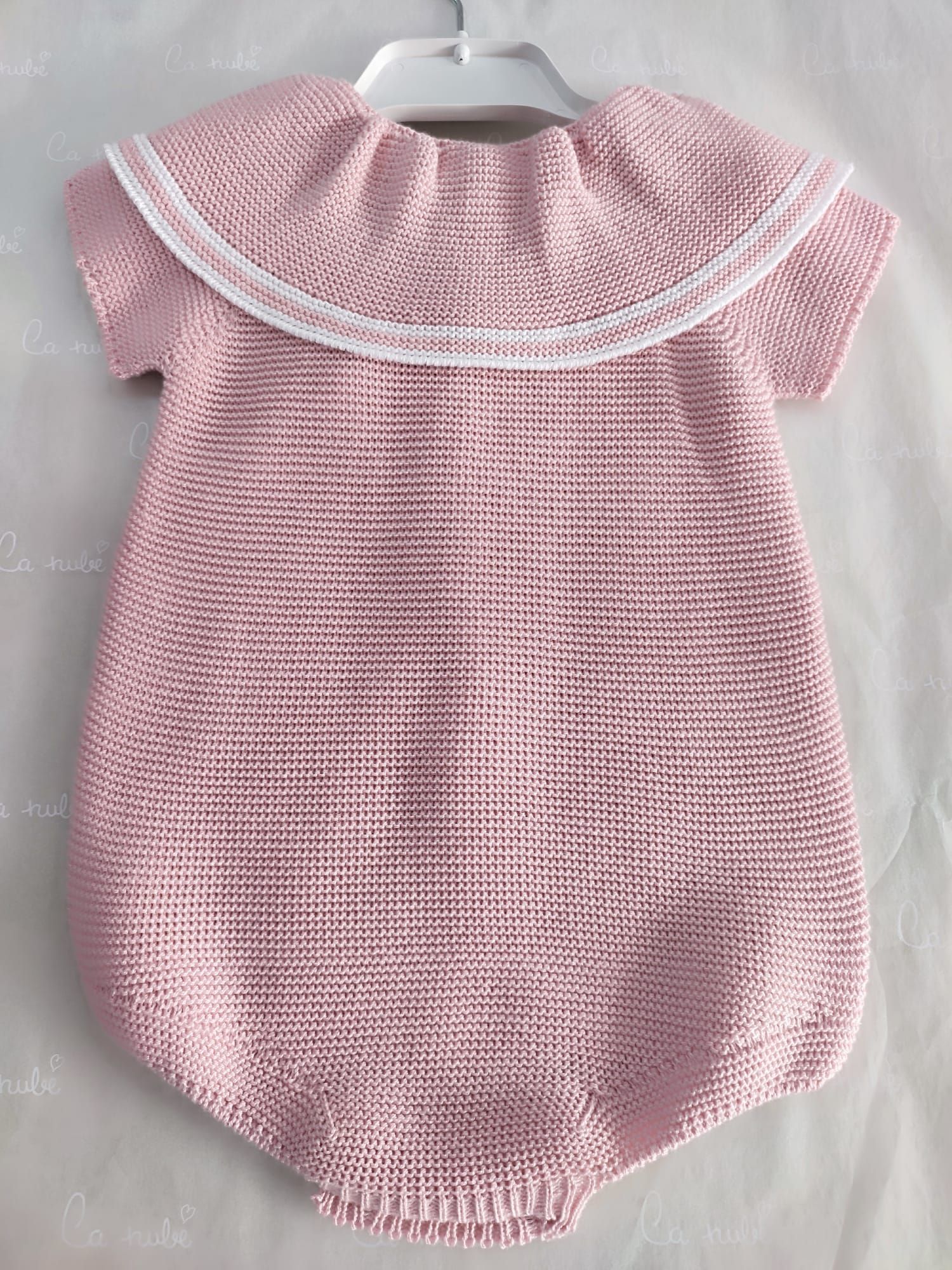 Un mono de bebé de punto rosa con cuello blanco está colgado en una percha.