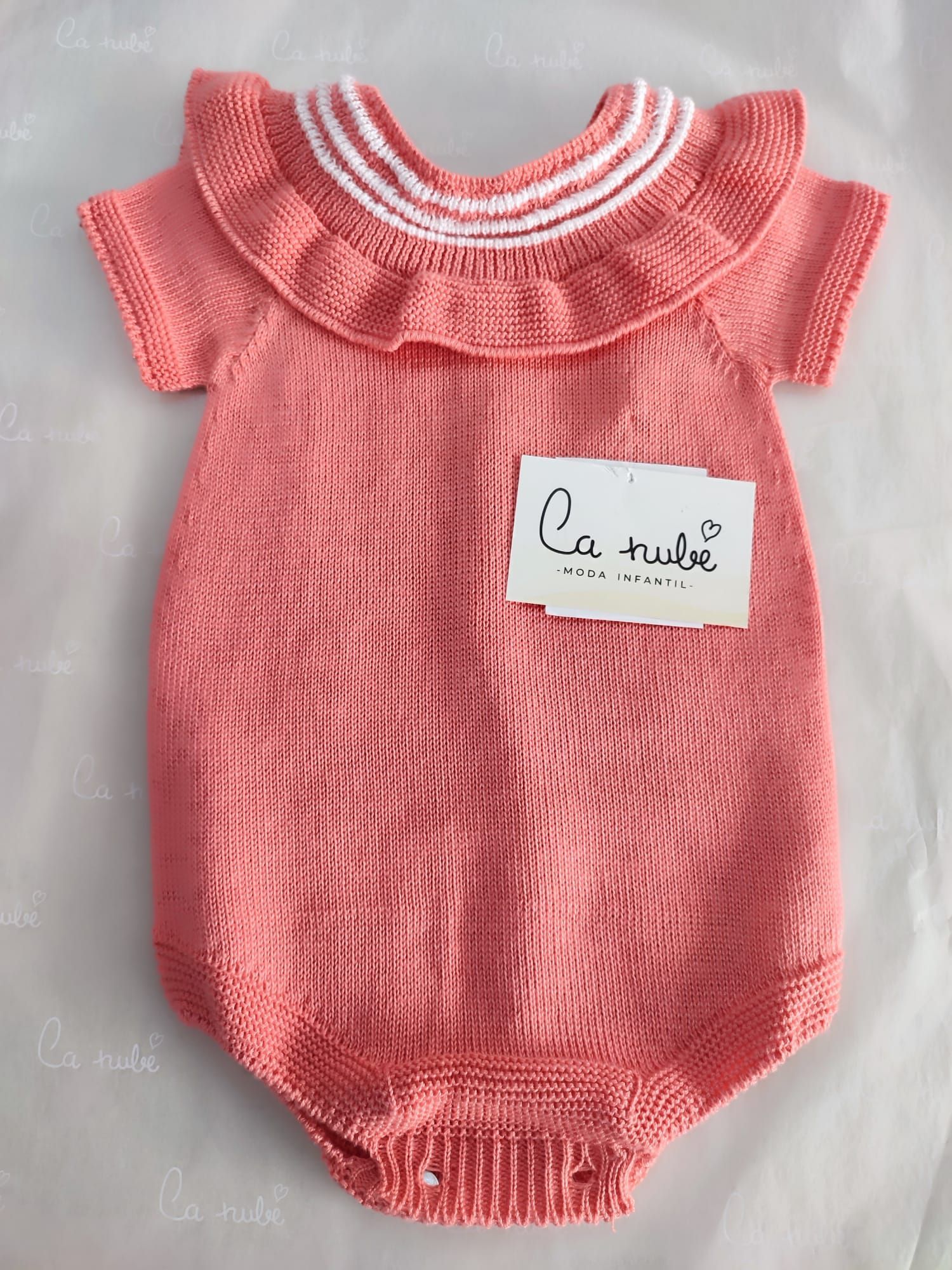 Un mono de bebé de punto rosa con cuello blanco y volantes.