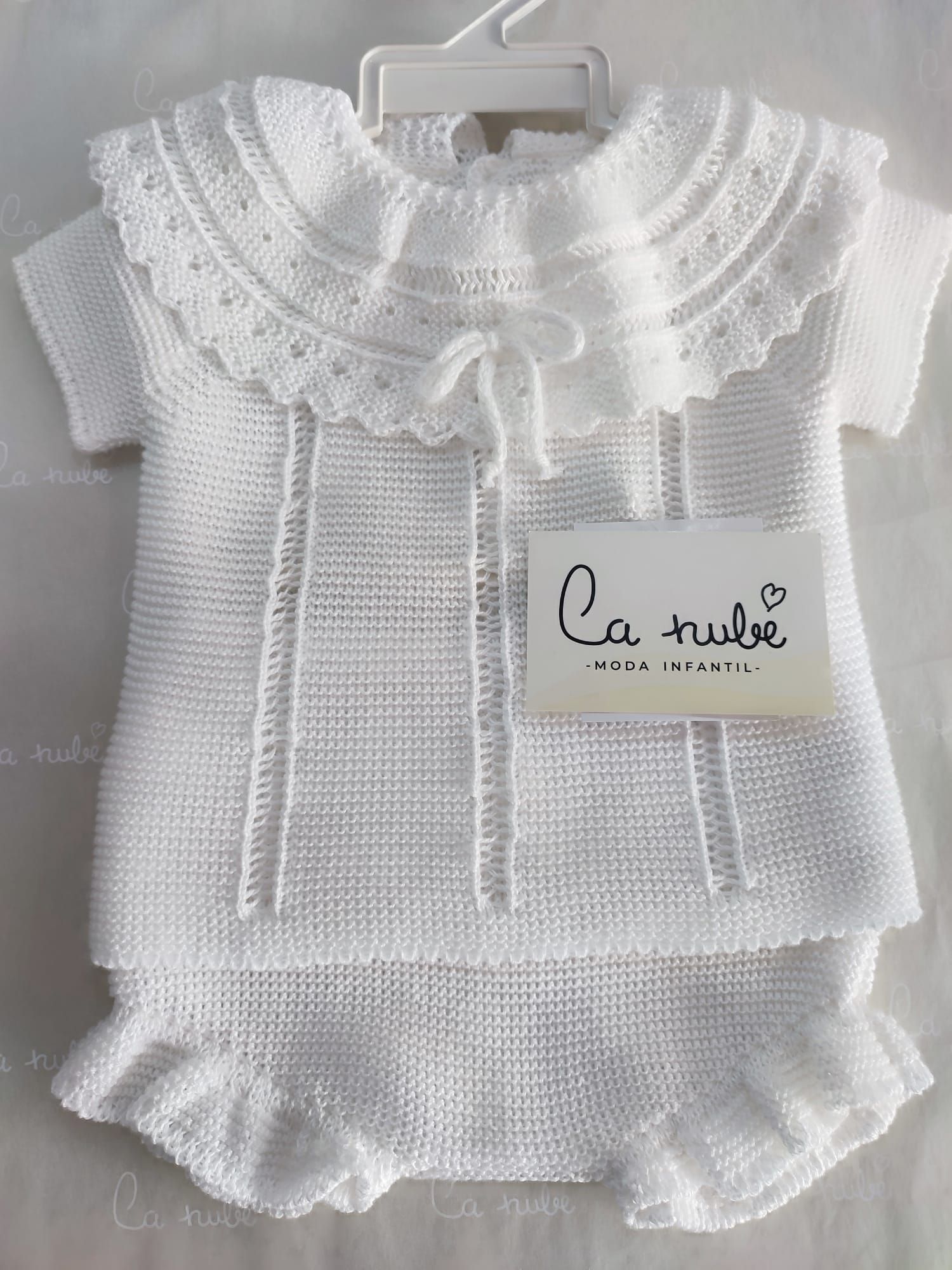 Un conjunto de bebé de punto blanco está colgado en una percha.