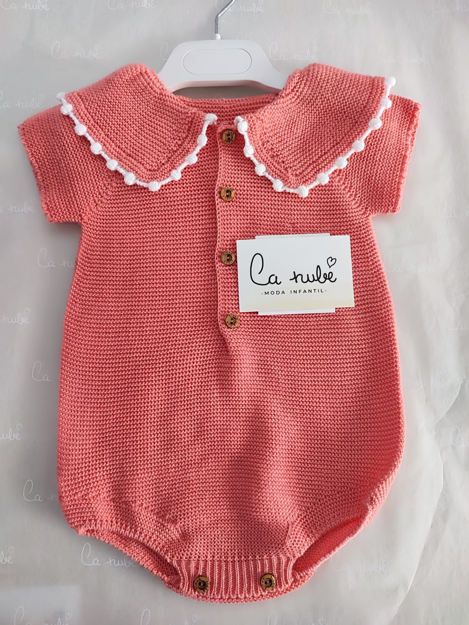 Un mono de bebé de punto rosa con cuello blanco.