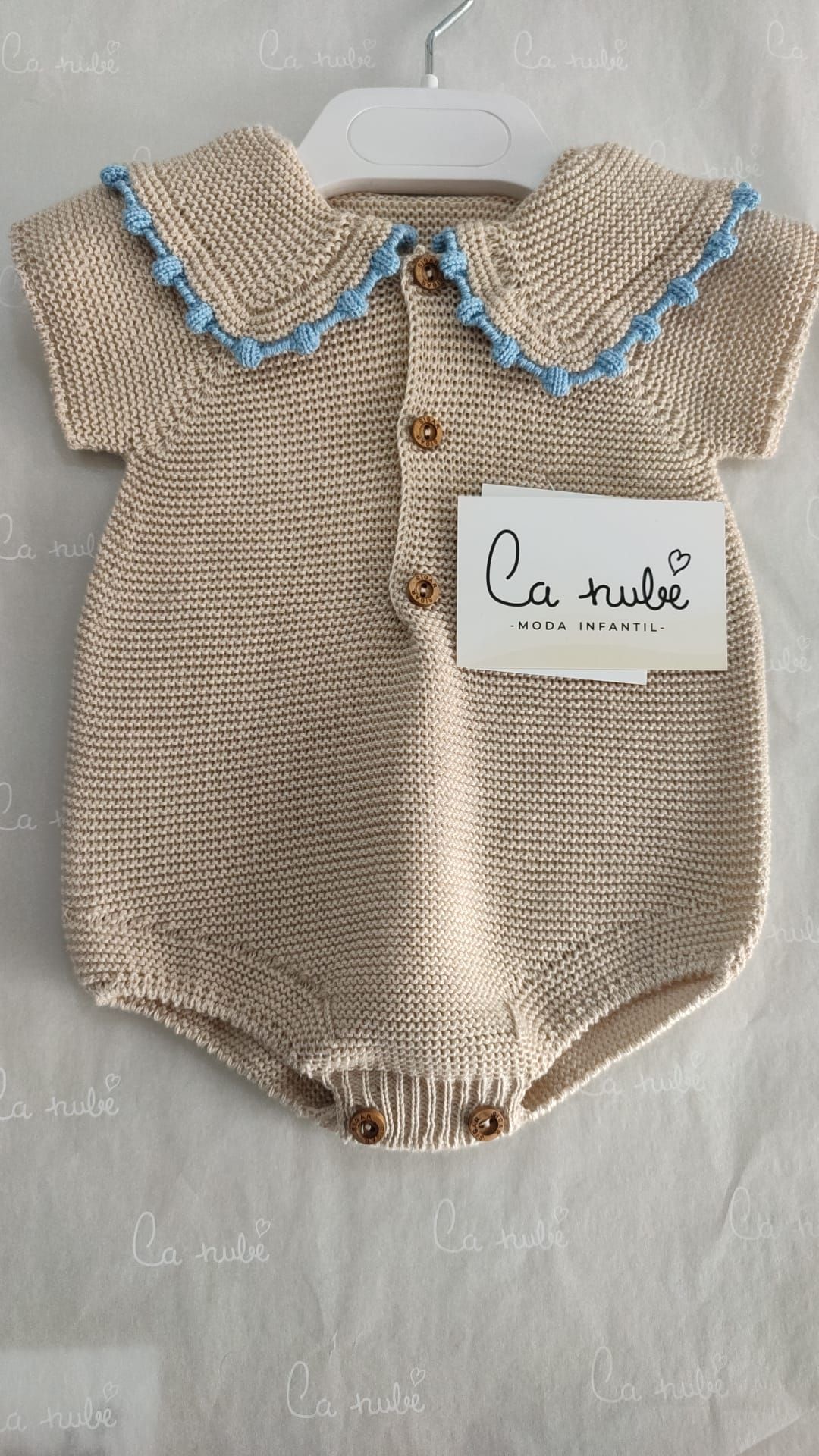 Un mono de bebé con cuello azul está colgado en una percha.