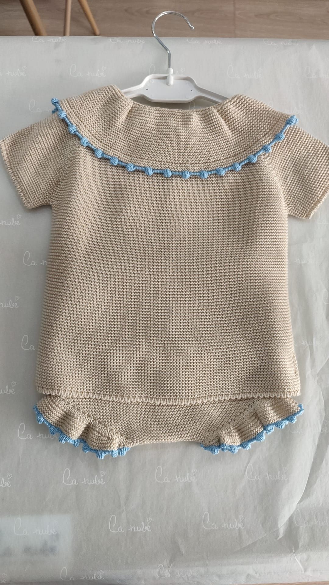 Un vestido de bebé tejido está colgado en una percha sobre una mesa.