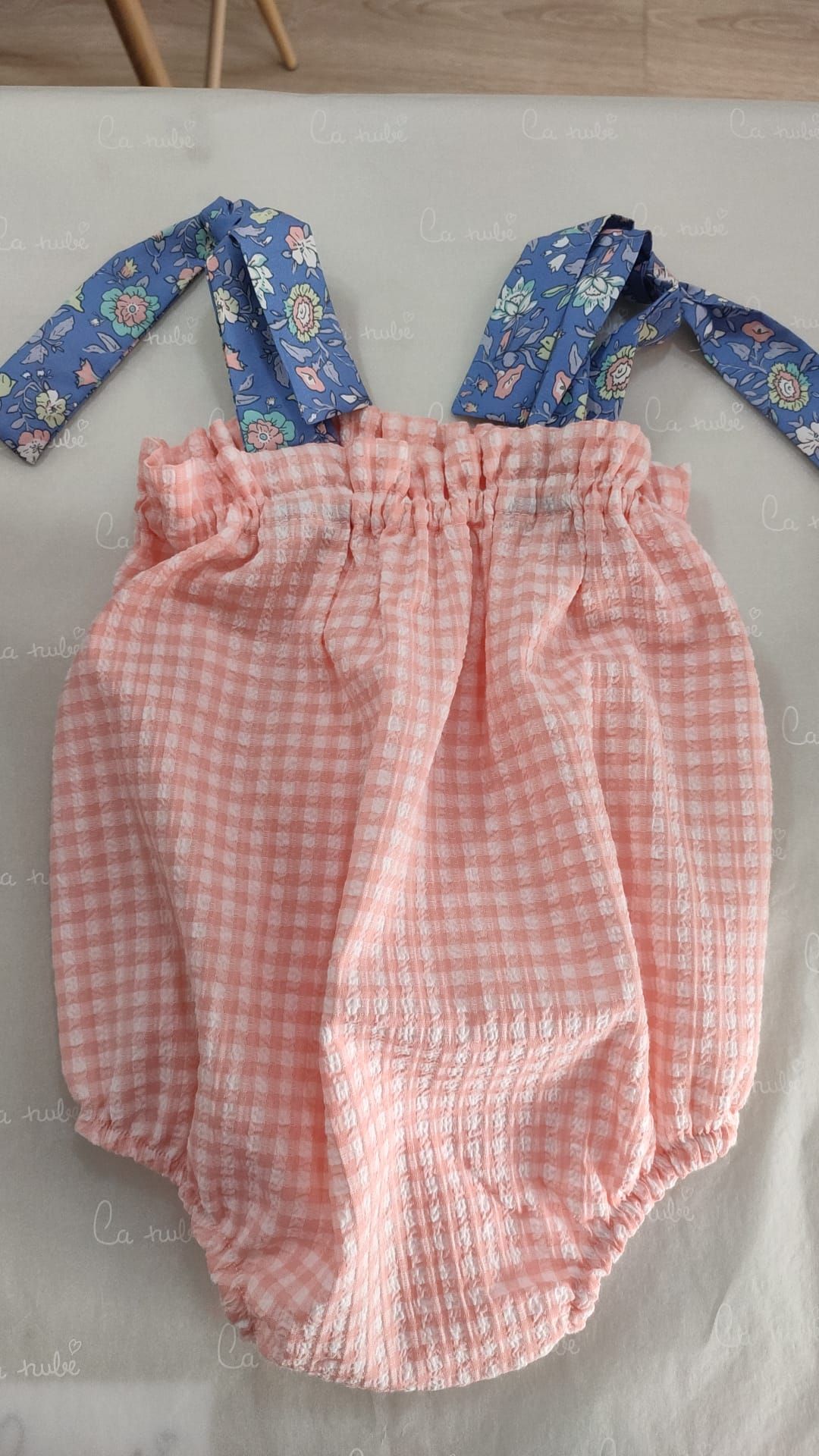 Un mono de bebé a cuadros rosa y azul con tirantes azules está sobre una mesa.